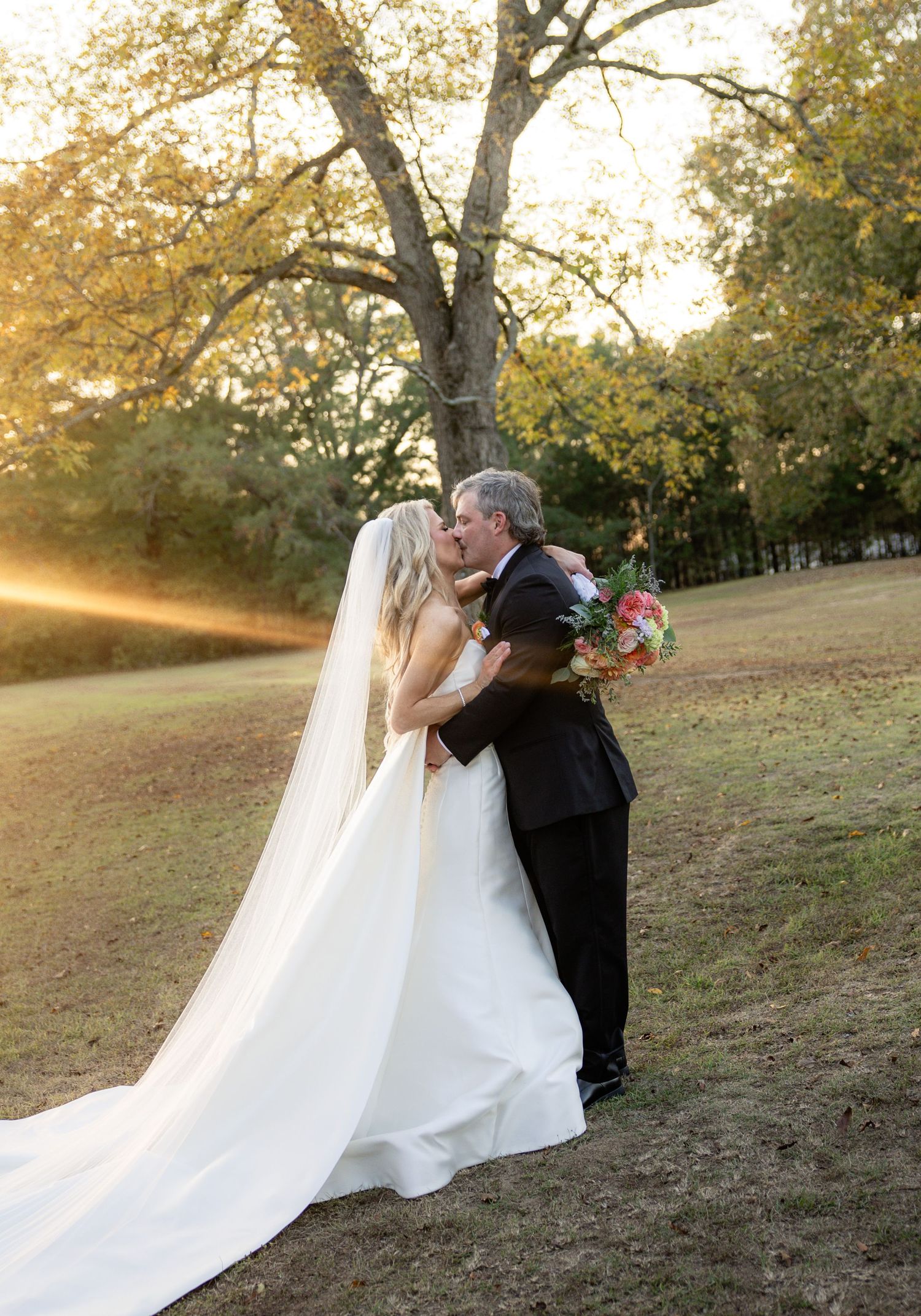 Romantic sunset wedding portraits captured on a hillside with autumn trees and flowing veil in golden light.