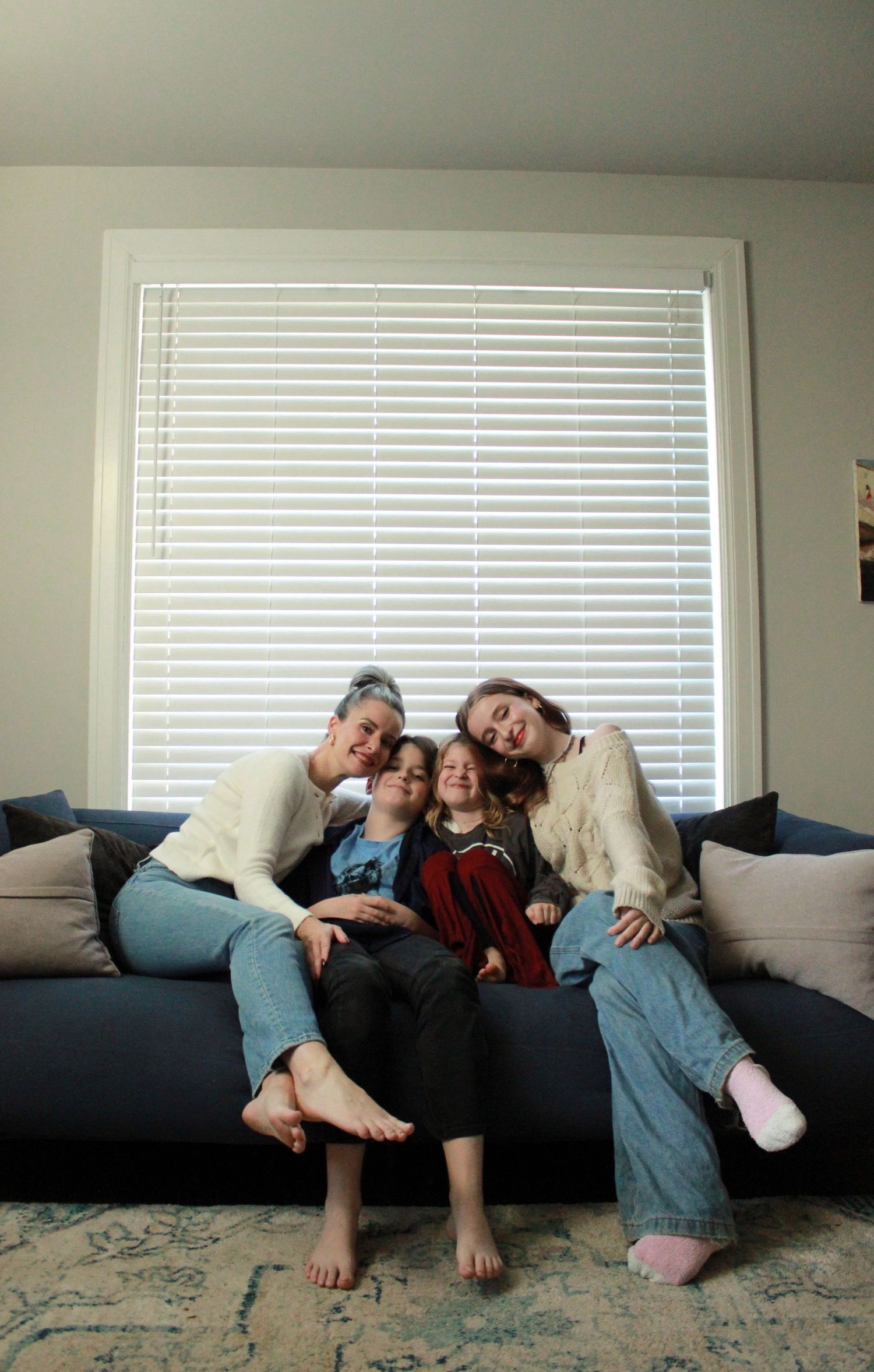 Family relaxing together on gray couch in front of window with white blinds.