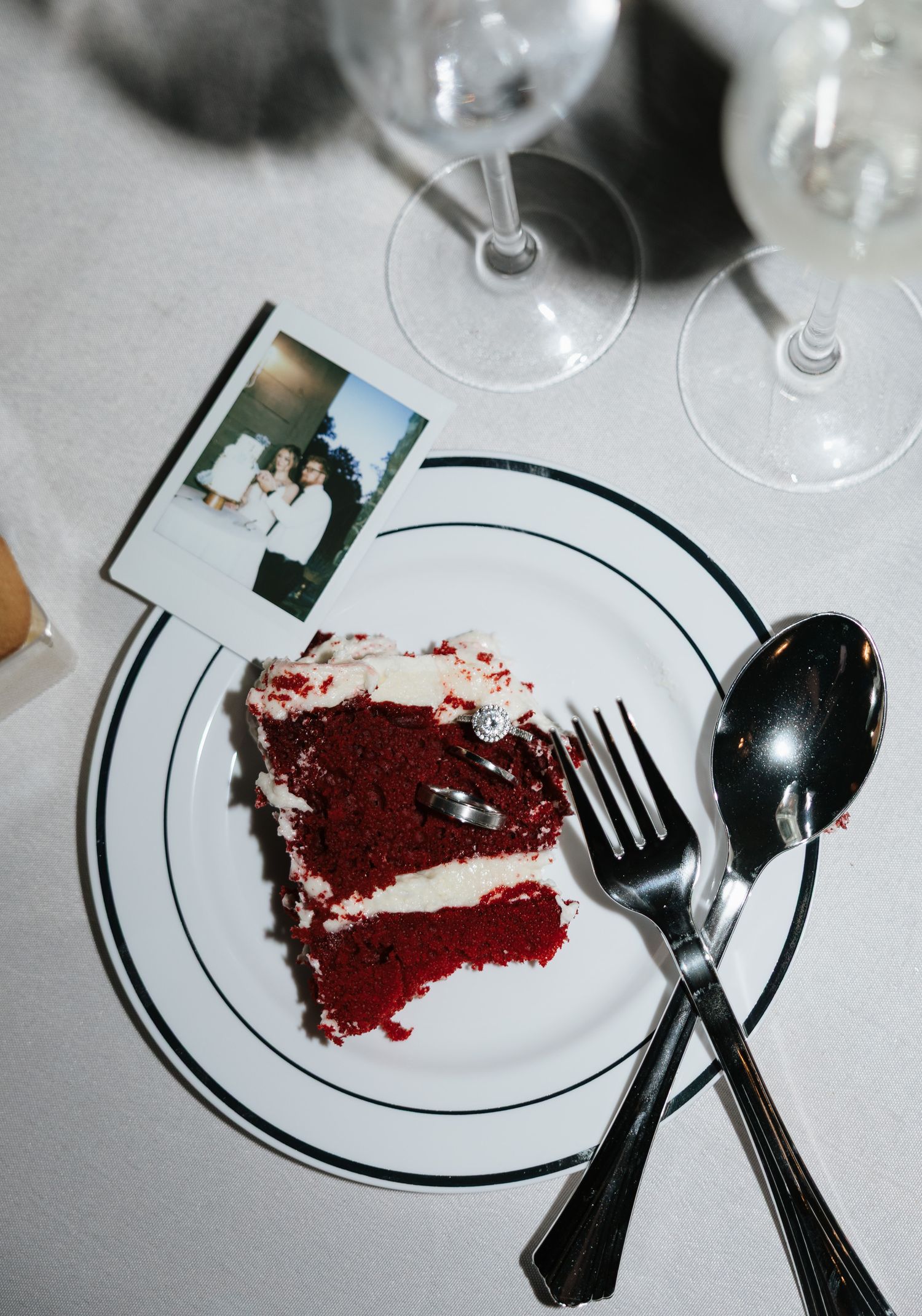 Slice of red velvet wedding cake on plate with fork and spoon next to a Polaroid photo.