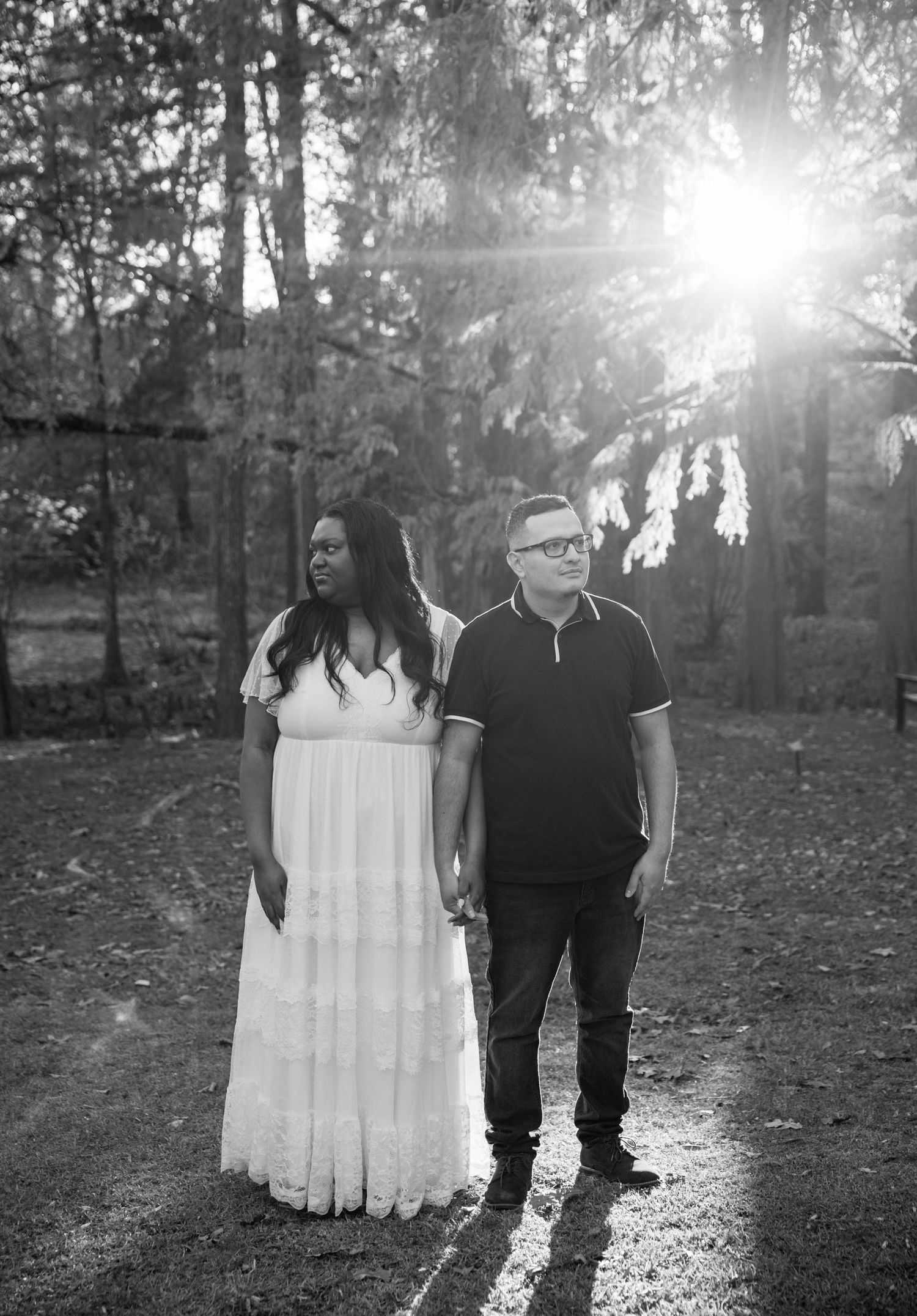Black and white outdoor photo series showing couple standing together in sunlit wooded area with romantic backlight.