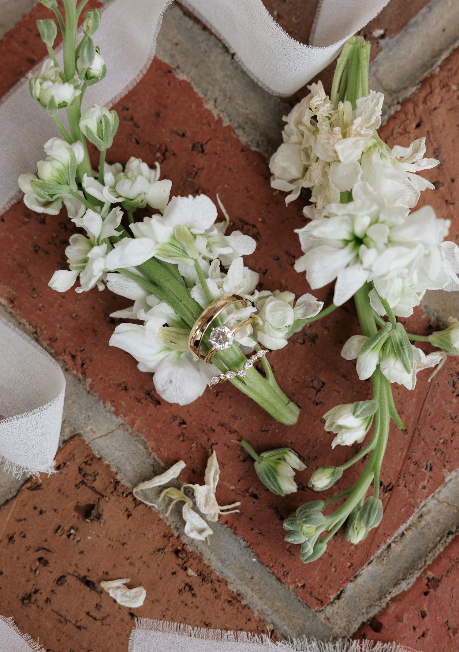 Wedding rings resting on white hyacinth boutonnieres placed on rustic red brick surface with silk ribbon.