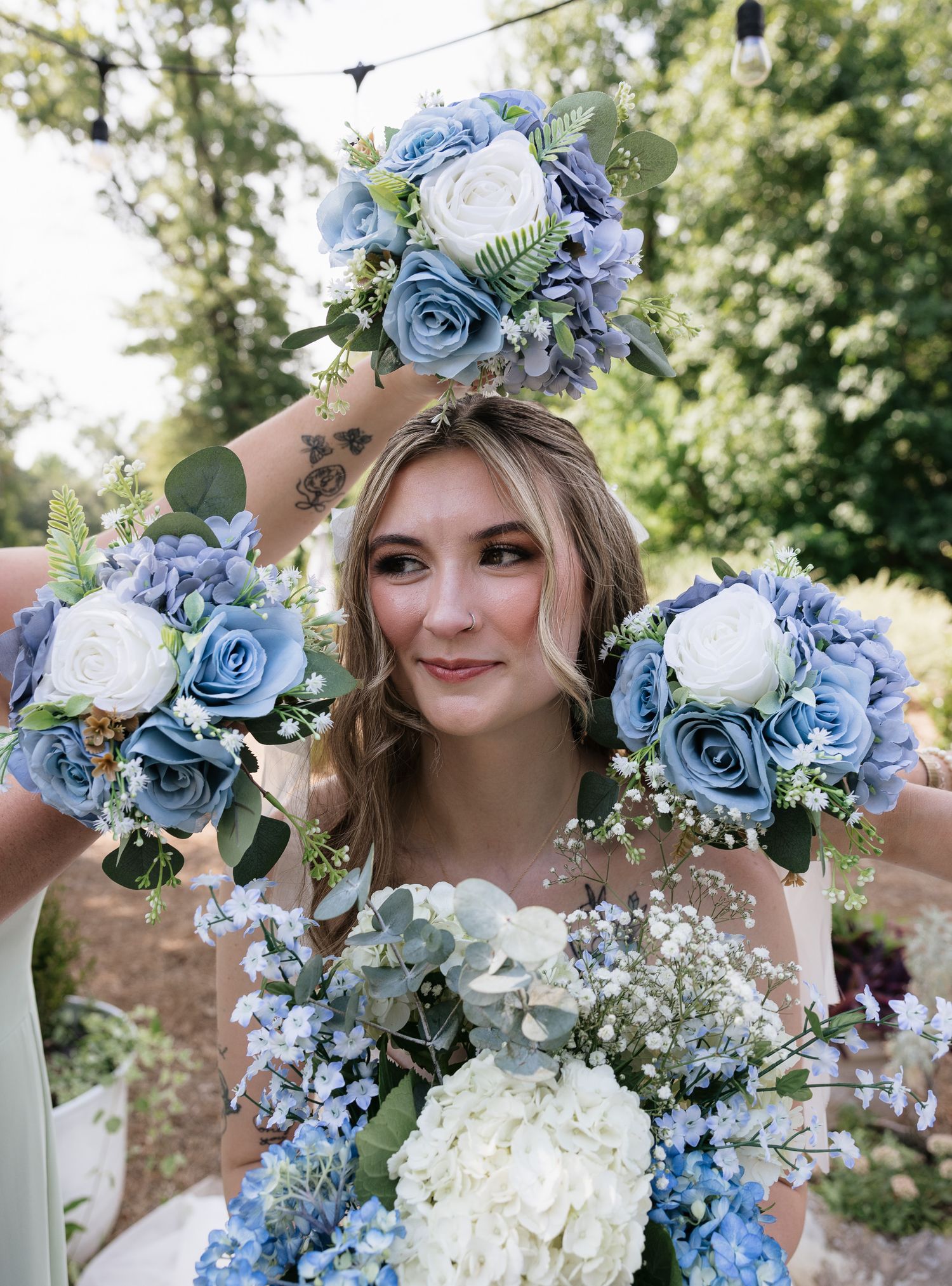 Bride holds multiple blue and white rose bouquets with hydrangeas and eucalyptus at an outdoor wedding.