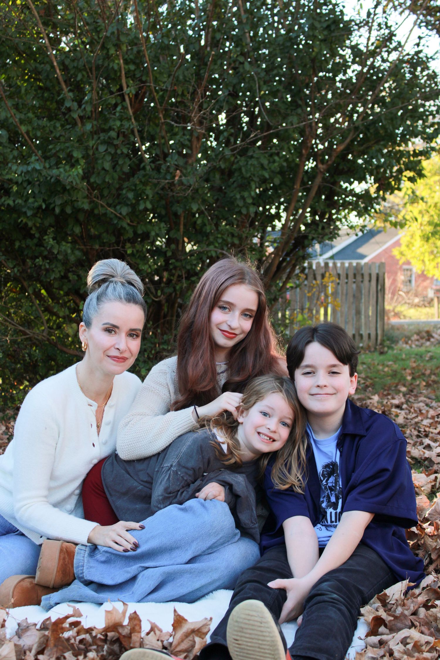 Friends lying together on fallen autumn leaves in a backyard setting.