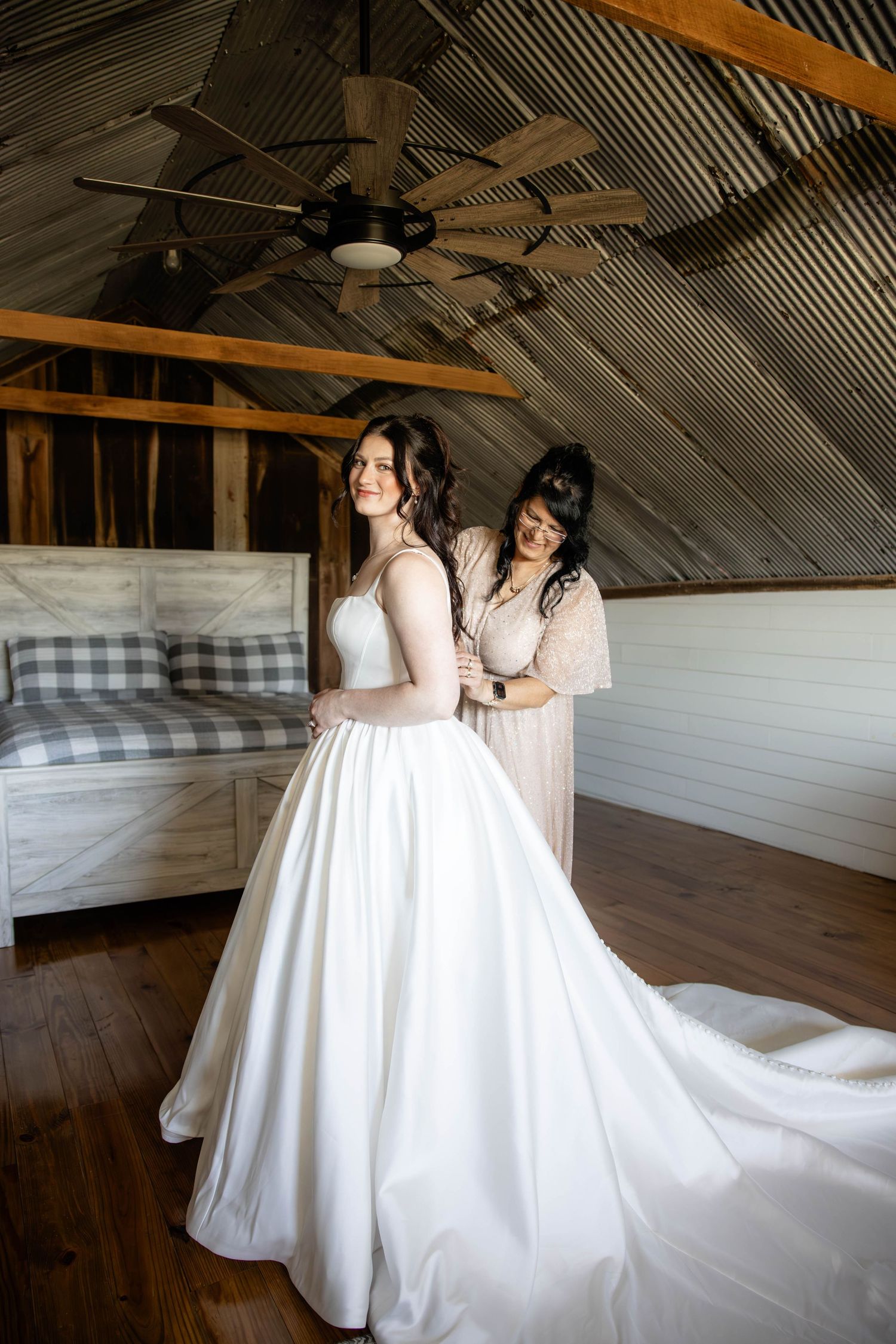 Two wedding gowns with flowing trains in rustic wooden attic setting.