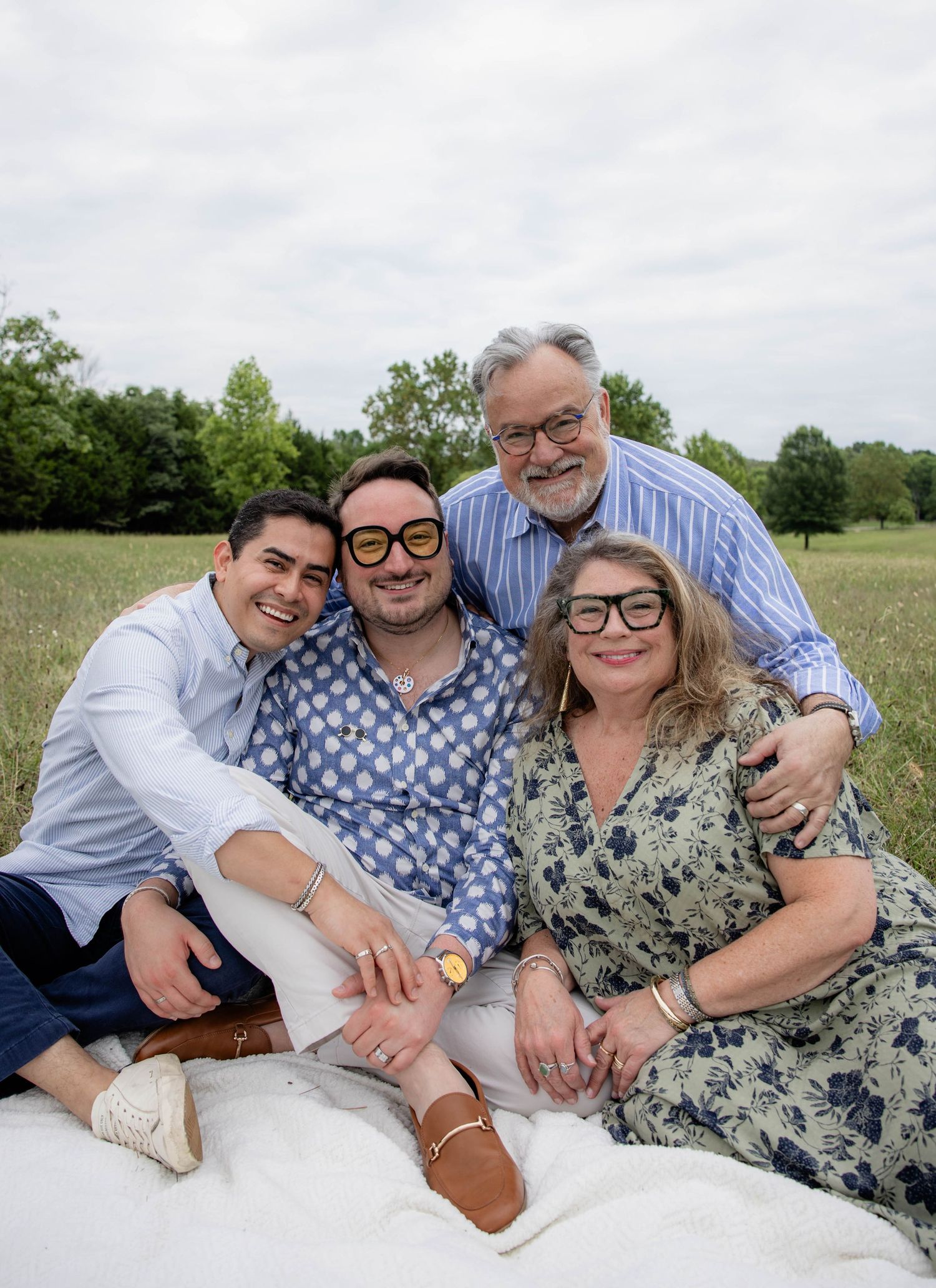 Family relaxing together on white blanket during outdoor photo session.