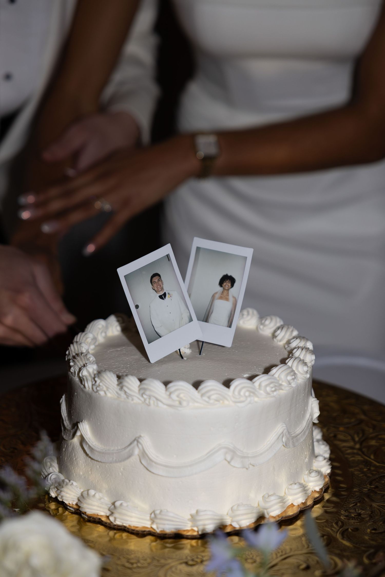 A white frosted wedding cake with small photo decorations being placed on top of it.
