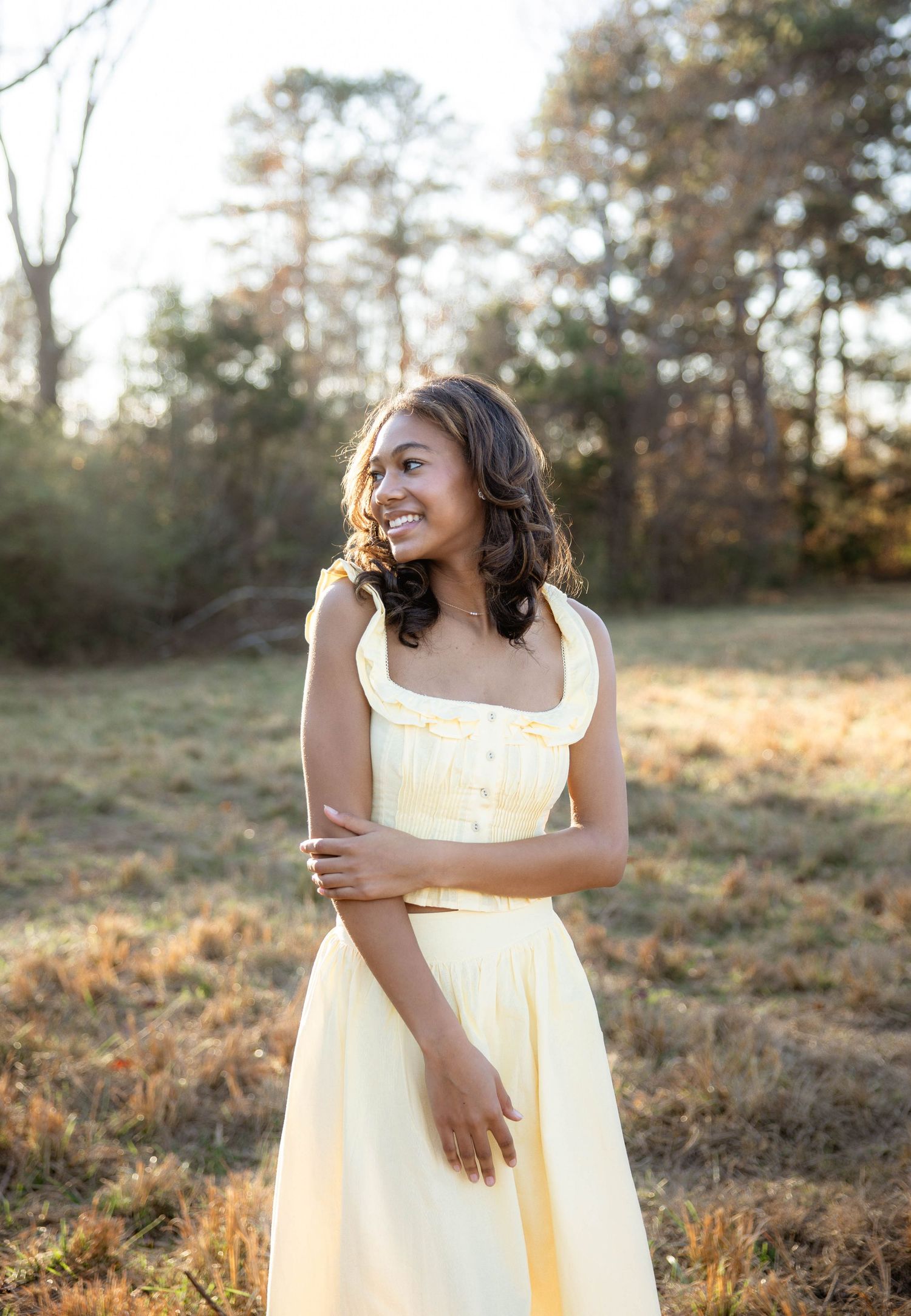 A person in a yellow dress poses in a sunlit field during golden hour.
