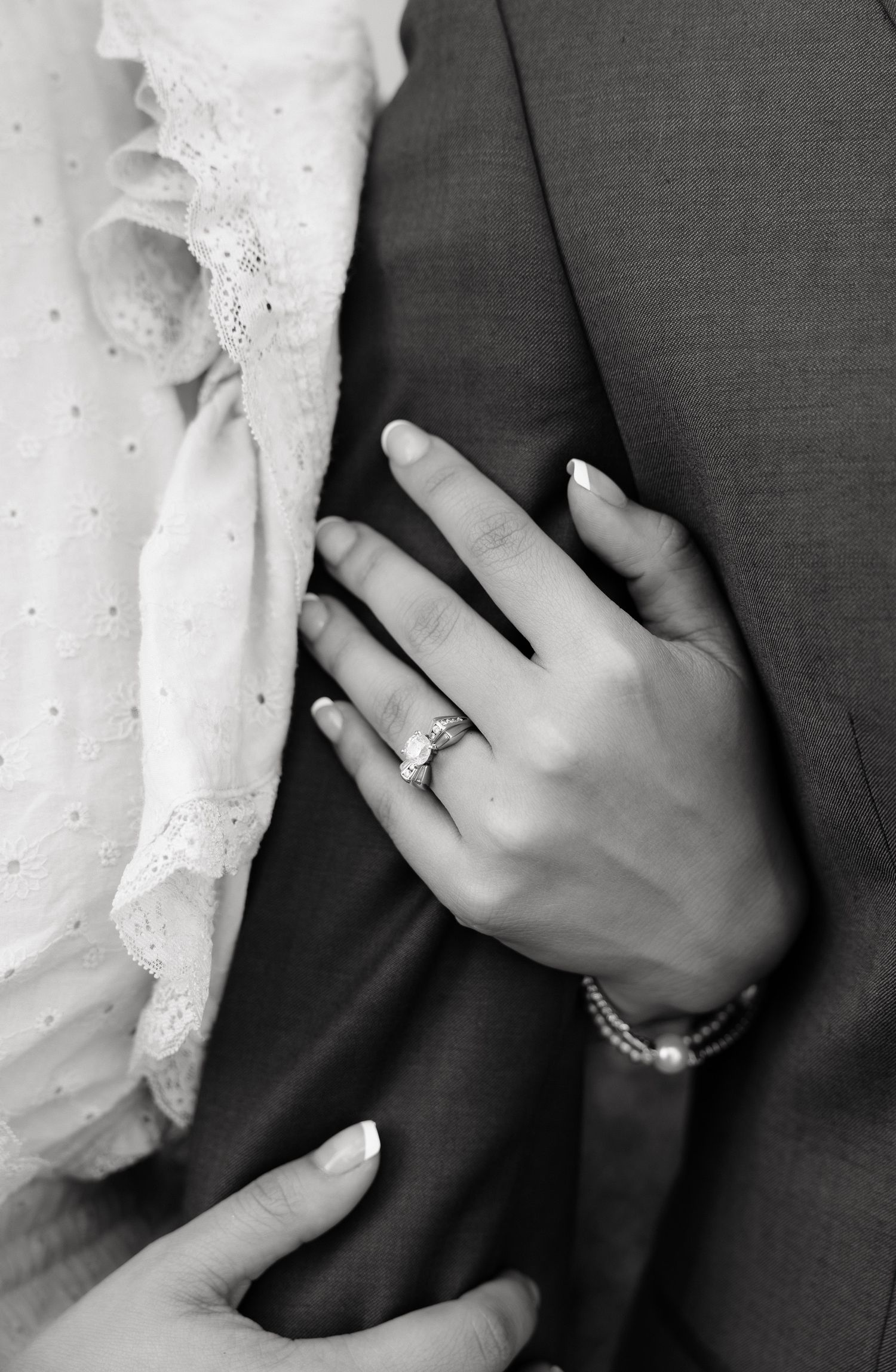 Black and white photo of bride's hand with wedding ring and bracelet resting on groom's suit jacket.