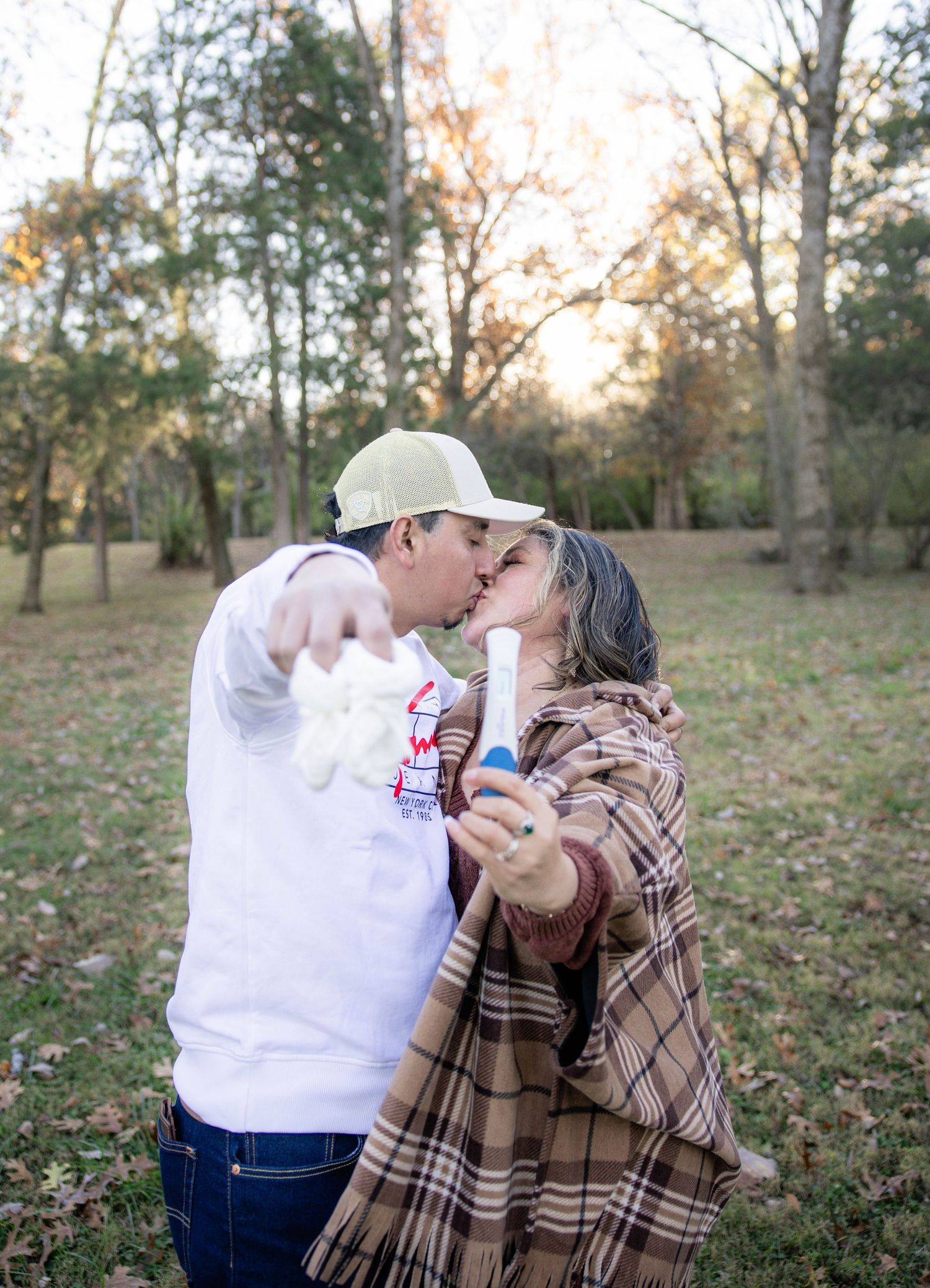 A couple shares a romantic moment outdoors in autumn, with the person in white embracing their partner in plaid.