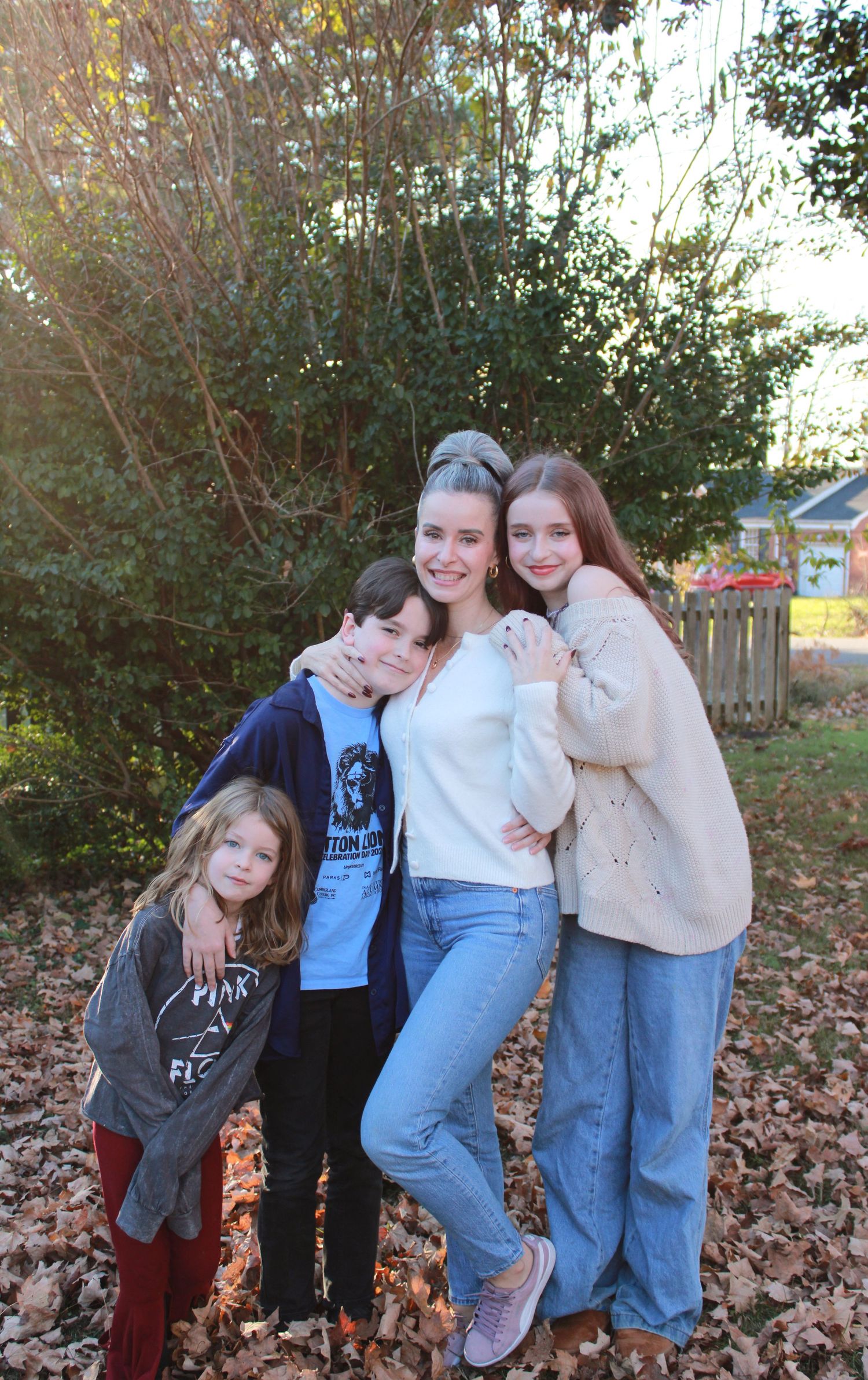 A casual group photo of friends posing together on fallen leaves in a backyard.