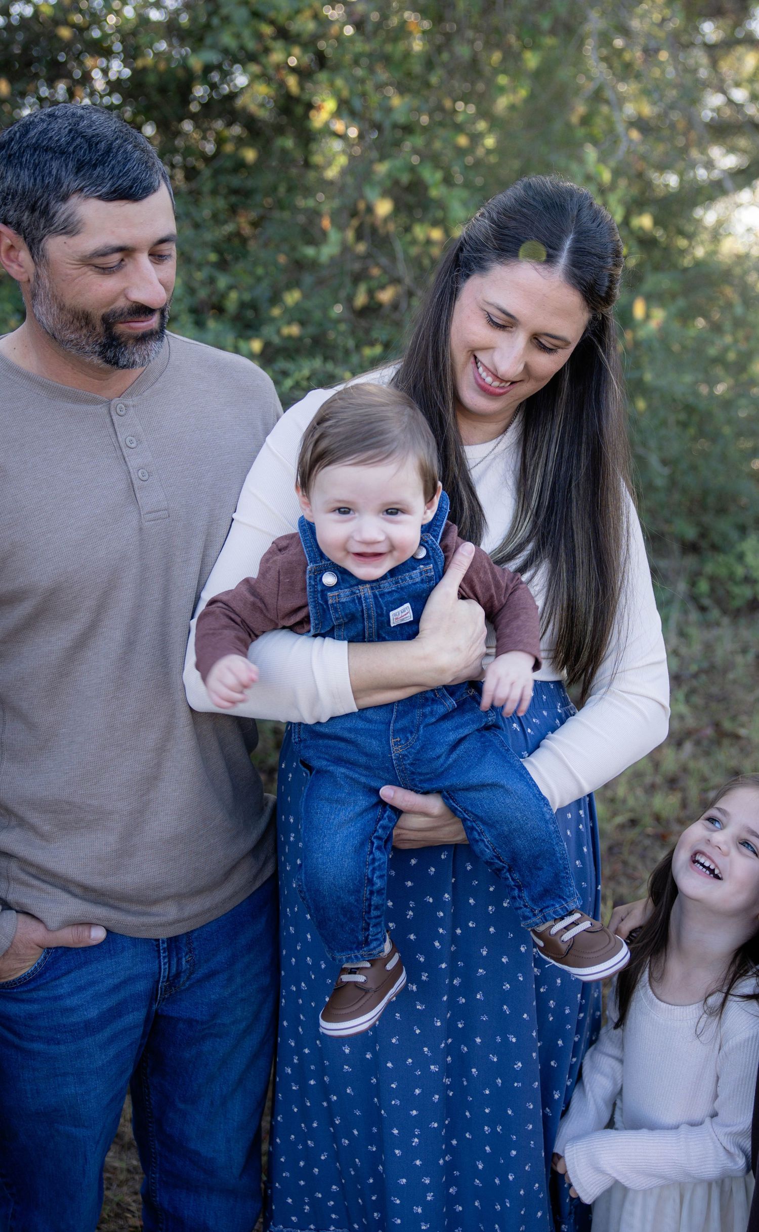 A family shares joyful moments together outdoors during a casual photo session in front of greenery.