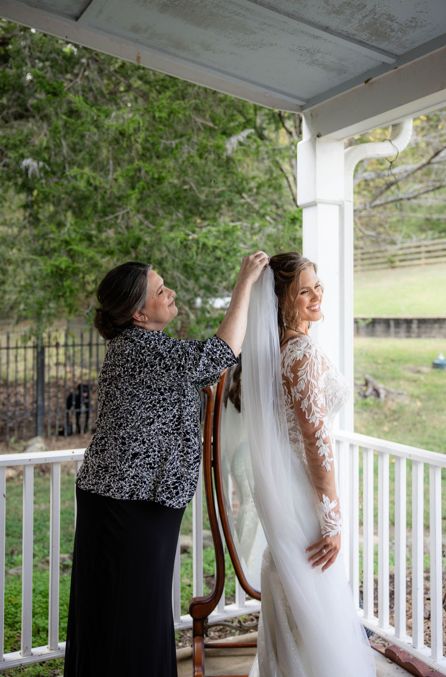 A wedding dress being prepared and adjusted on a covered porch with natural lighting.
