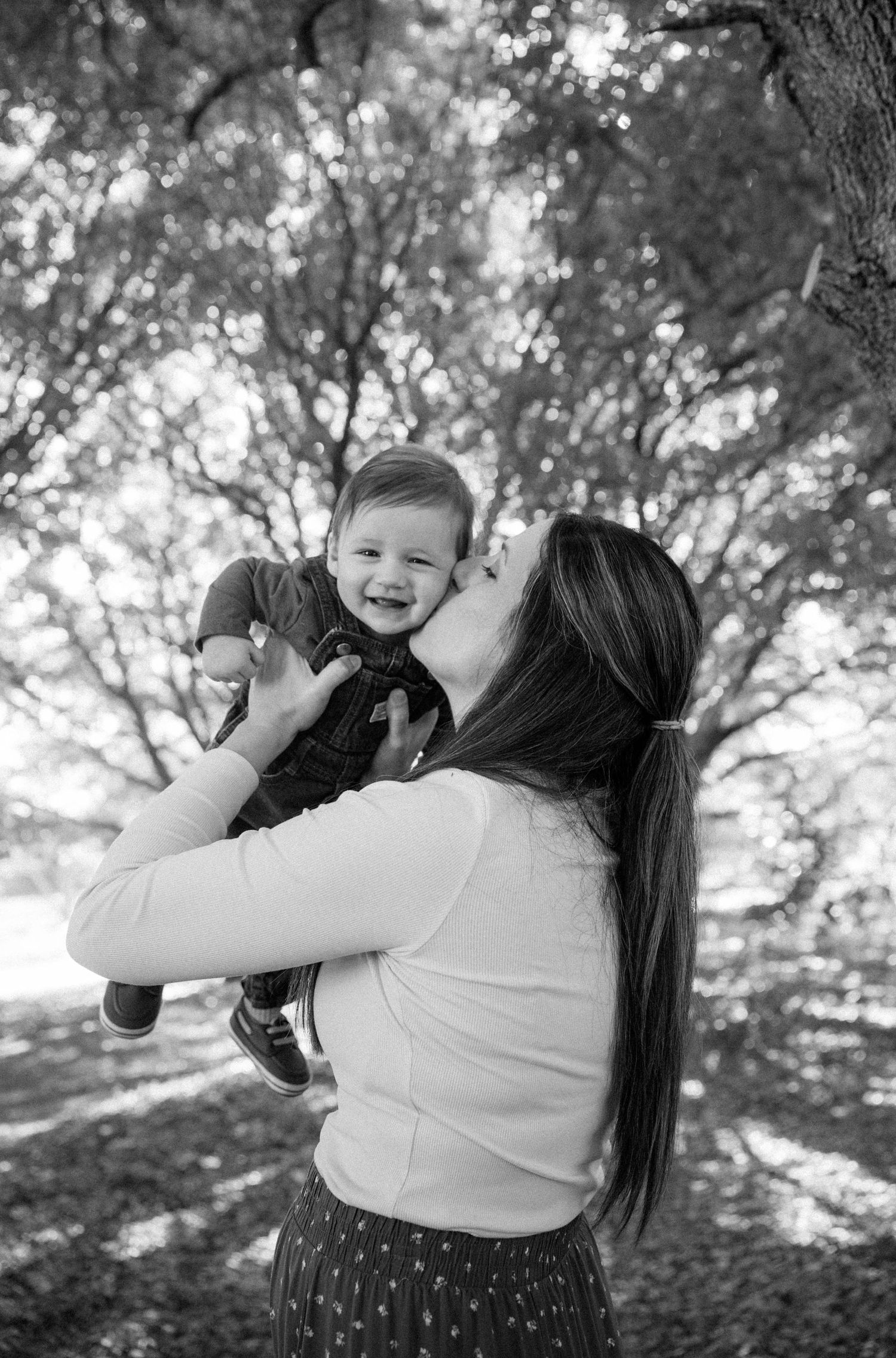 A series of black and white photos showing a playful moment between parent and child in a sunlit outdoor setting.
