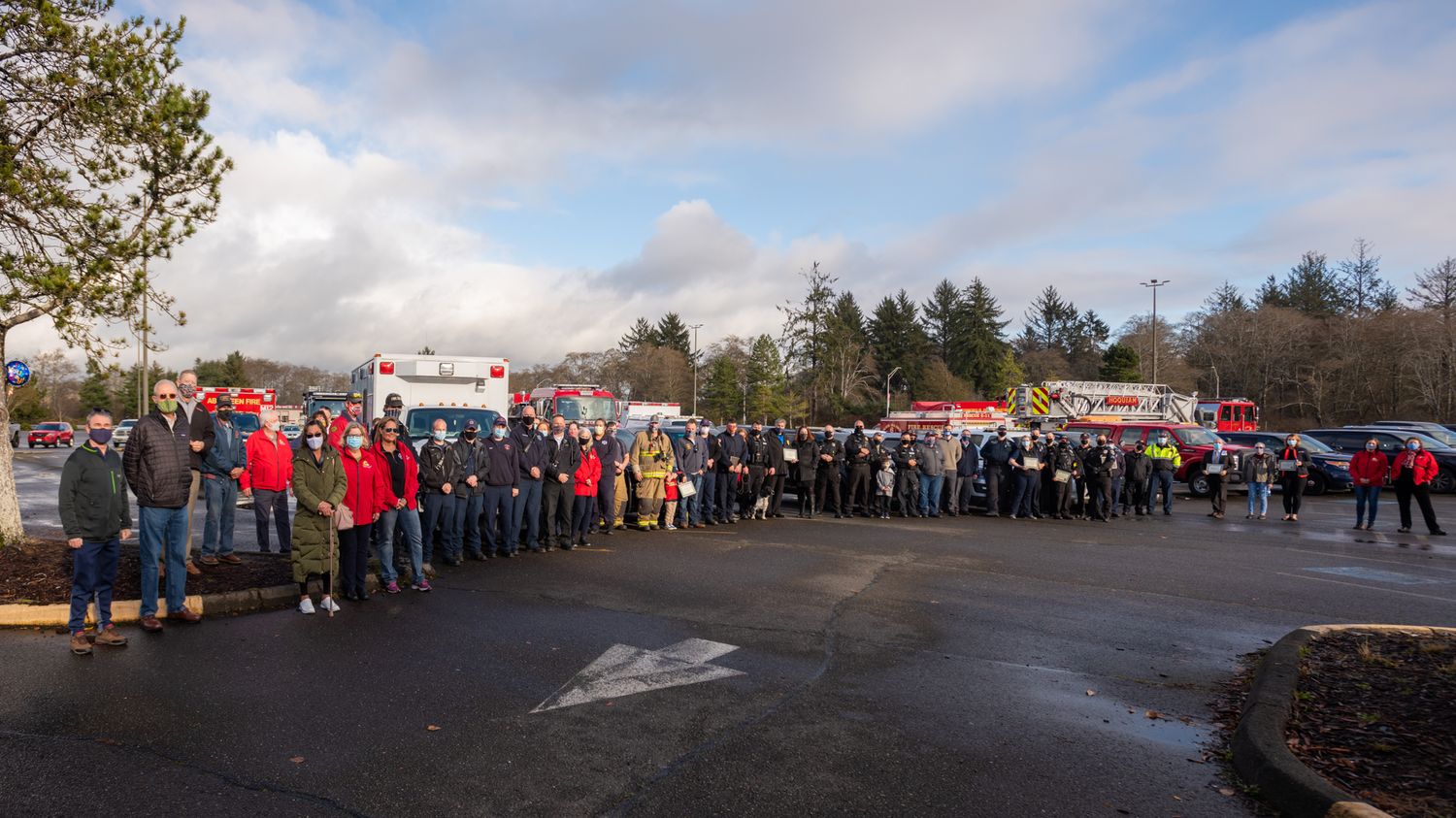 A large crowd of first responders and community members line up in a parking lot with ambulances and fire trucks behind them.