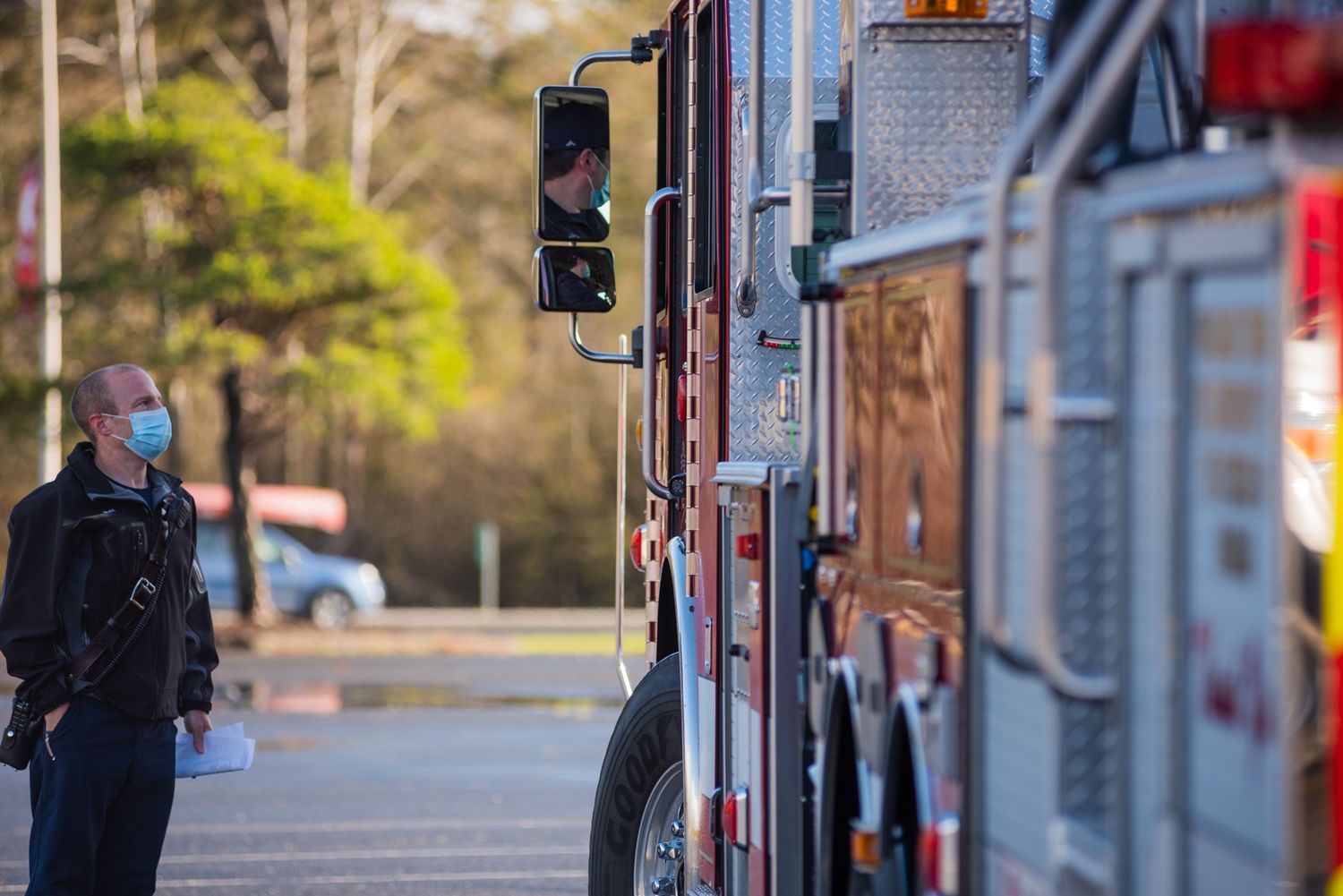 Masked man in a dark jacket stands in a parking lot facing a fire truck as the driver looks out the window.