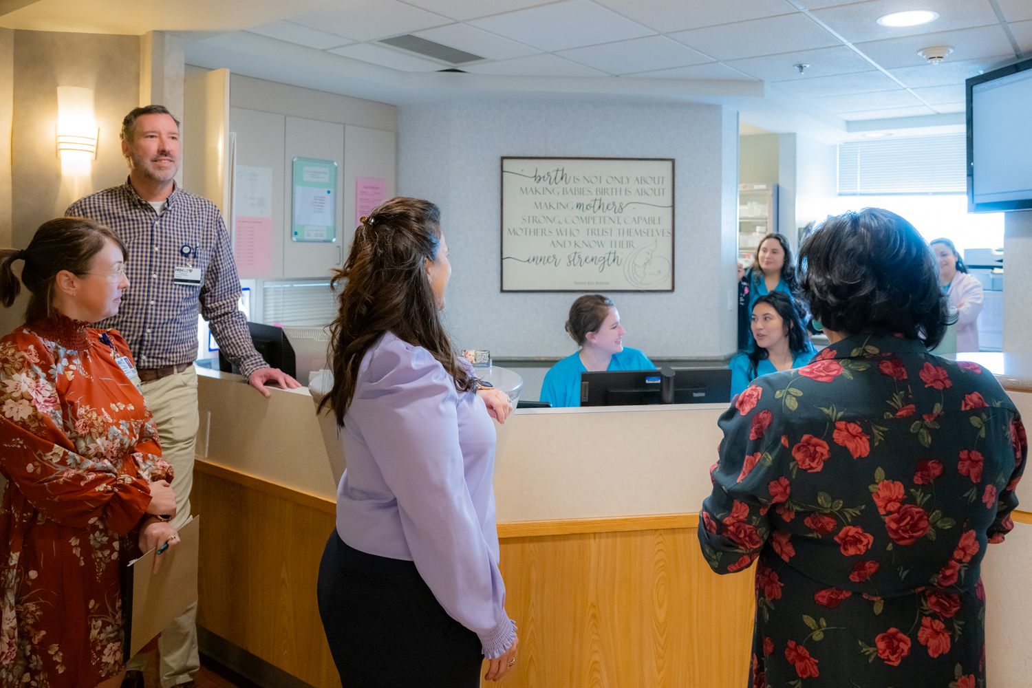 Group of people gathered at a wooden reception desk in a bright medical office while staff members seated behind the counter greet them.