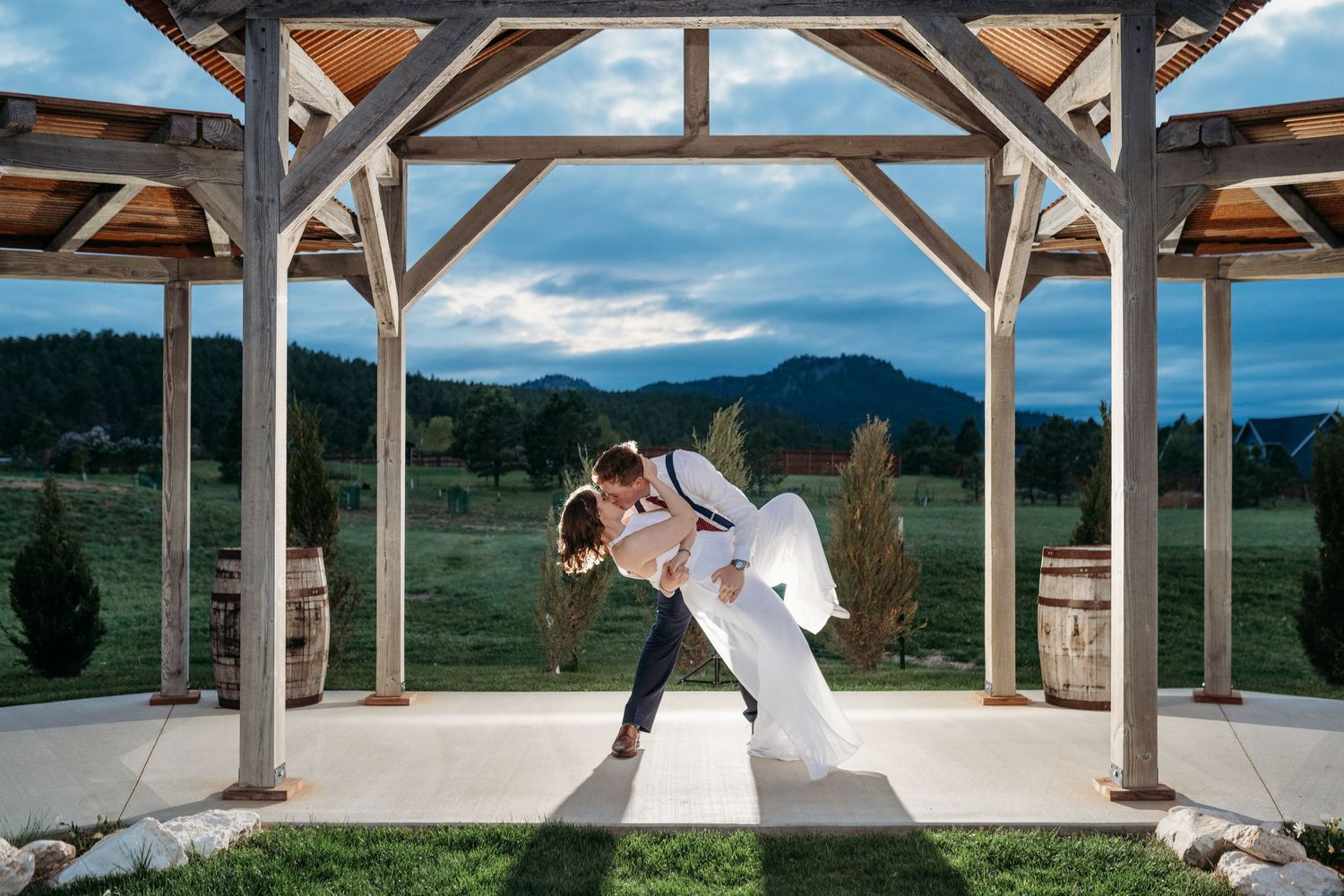 Romantic silhouette under a wooden pavilion with mountain views and dramatic cloudy sky at sunset.