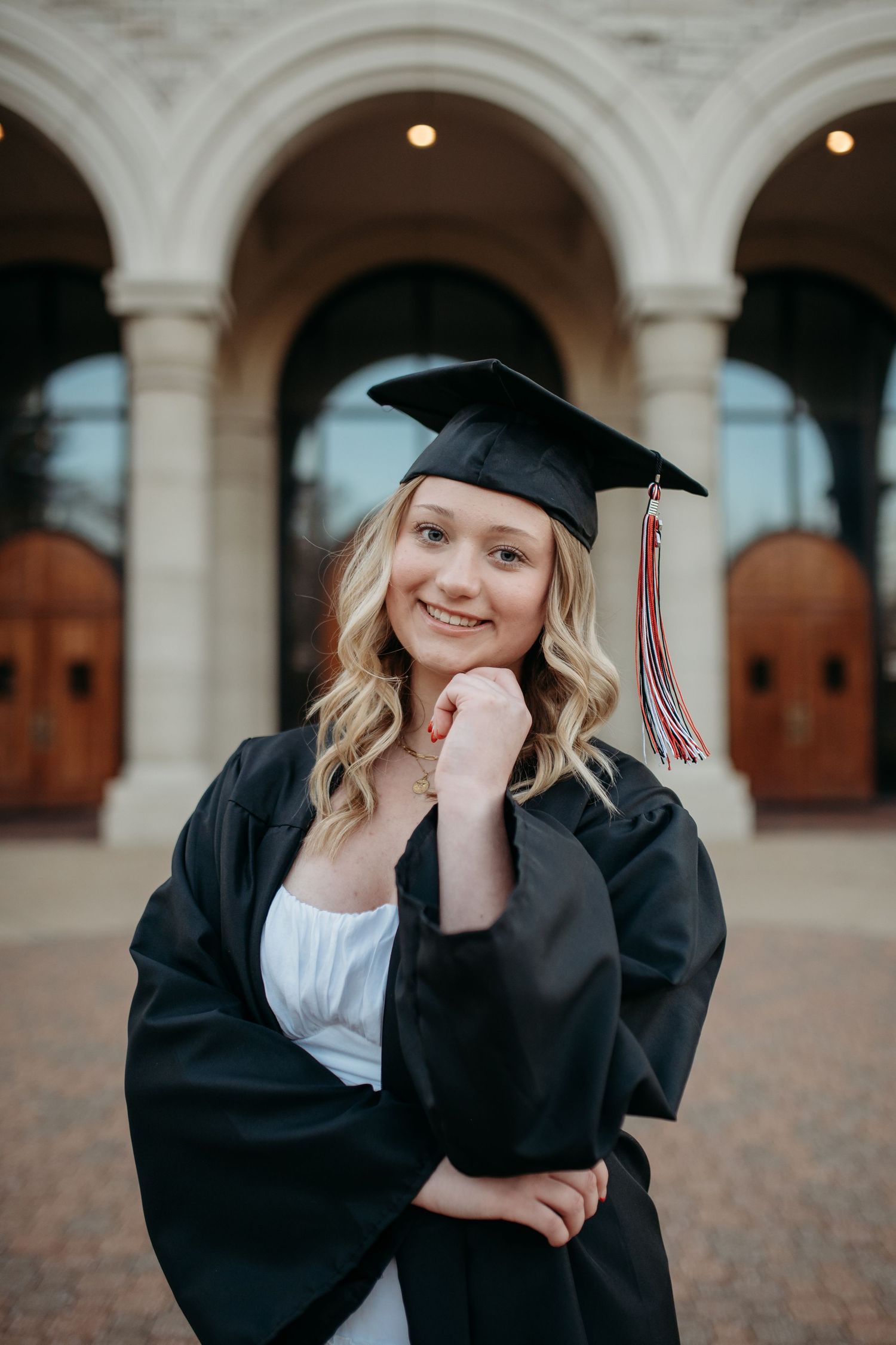 Graduate in cap and gown poses in front of stone architecture during outdoor portrait session at best places for senior photos in St. Louis