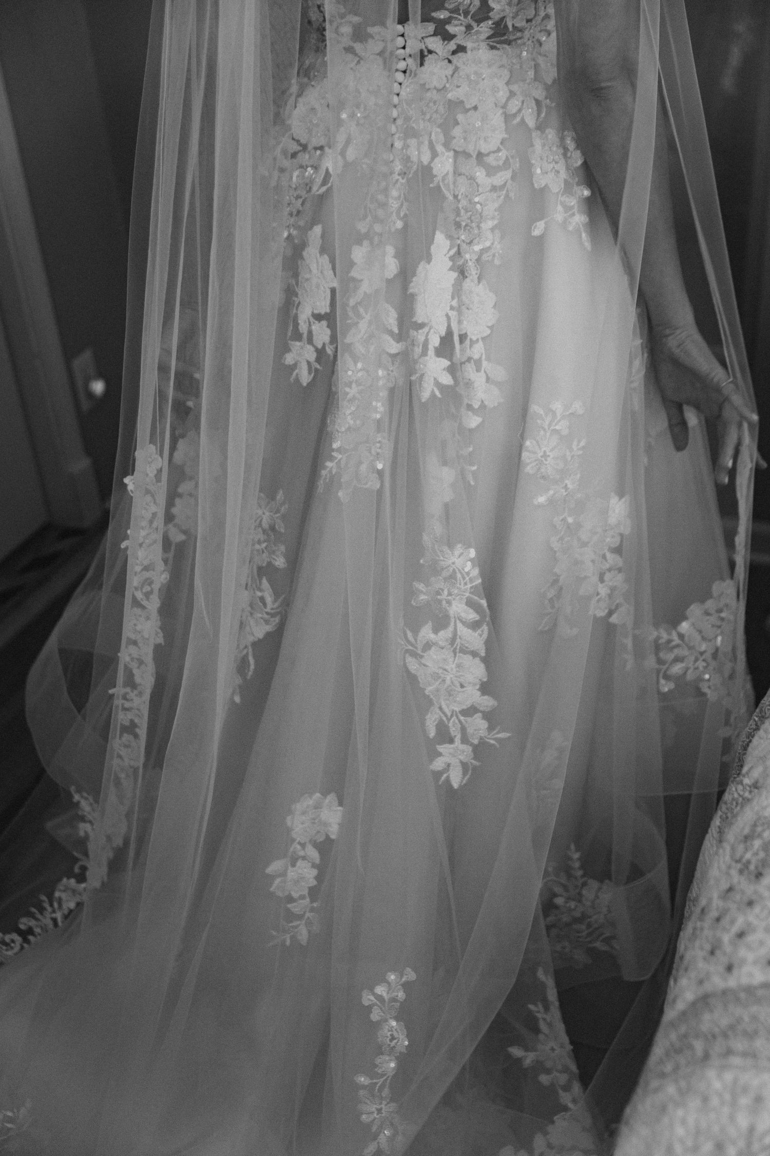 Black and white close-up of floral applique wedding gown with flowing tulle veil.