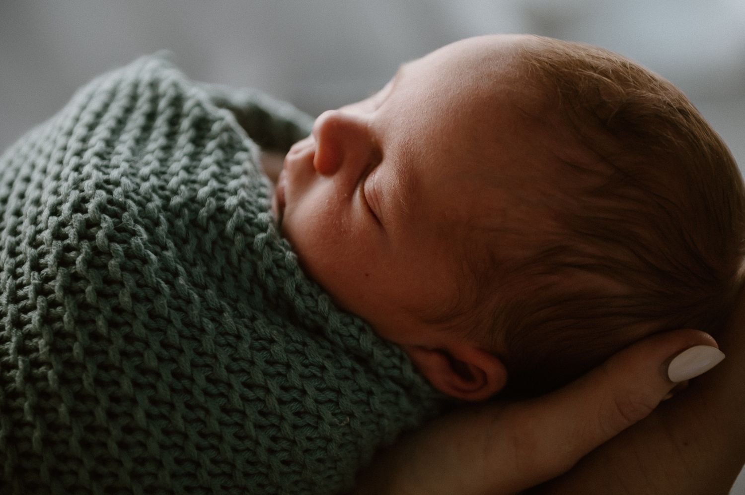Peaceful newborn baby sleeping swaddled in a soft green knit blanket for newborn photoshoot with Story&Soul Photography in Mandurah WA