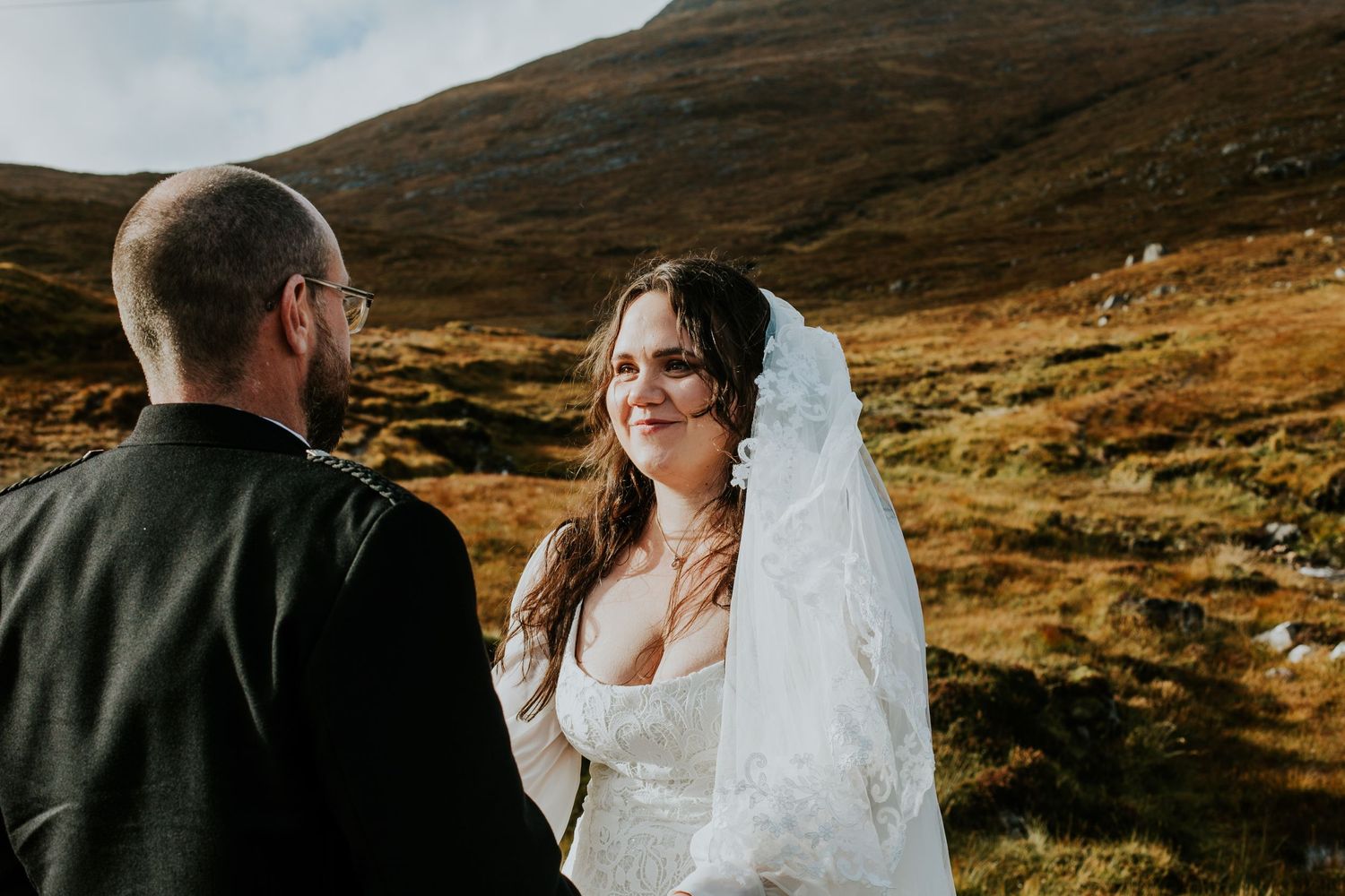 A couple shares an intimate moment against a backdrop of rolling Scottish highlands.