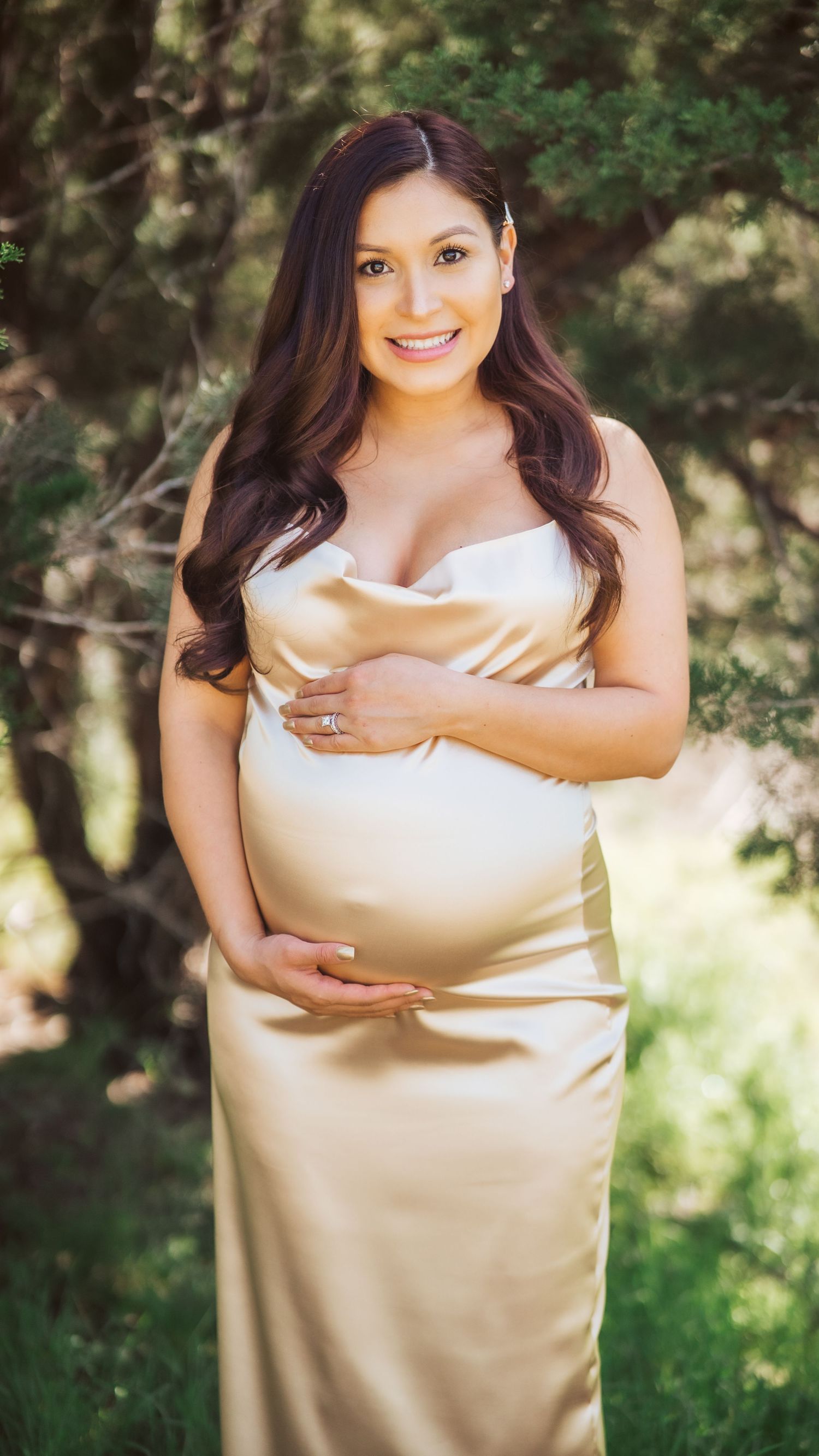 An outdoor maternity portrait showing an expectant mother in a champagne-colored satin gown.