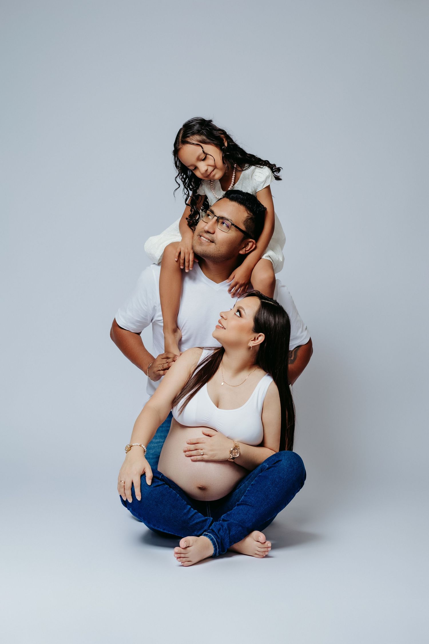 Studio family portrait with white and blue casual outfits against light grey background.
