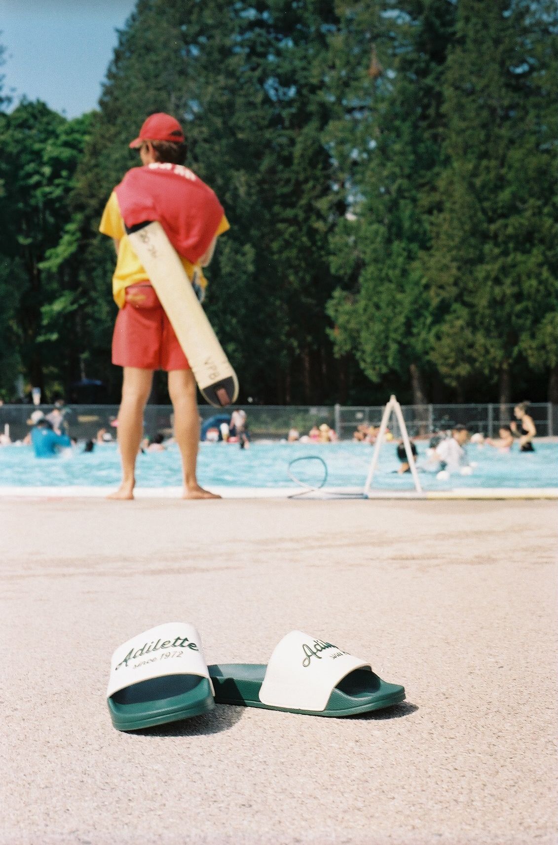 Lifeguard watching over public swimming pool with sandals in foreground.