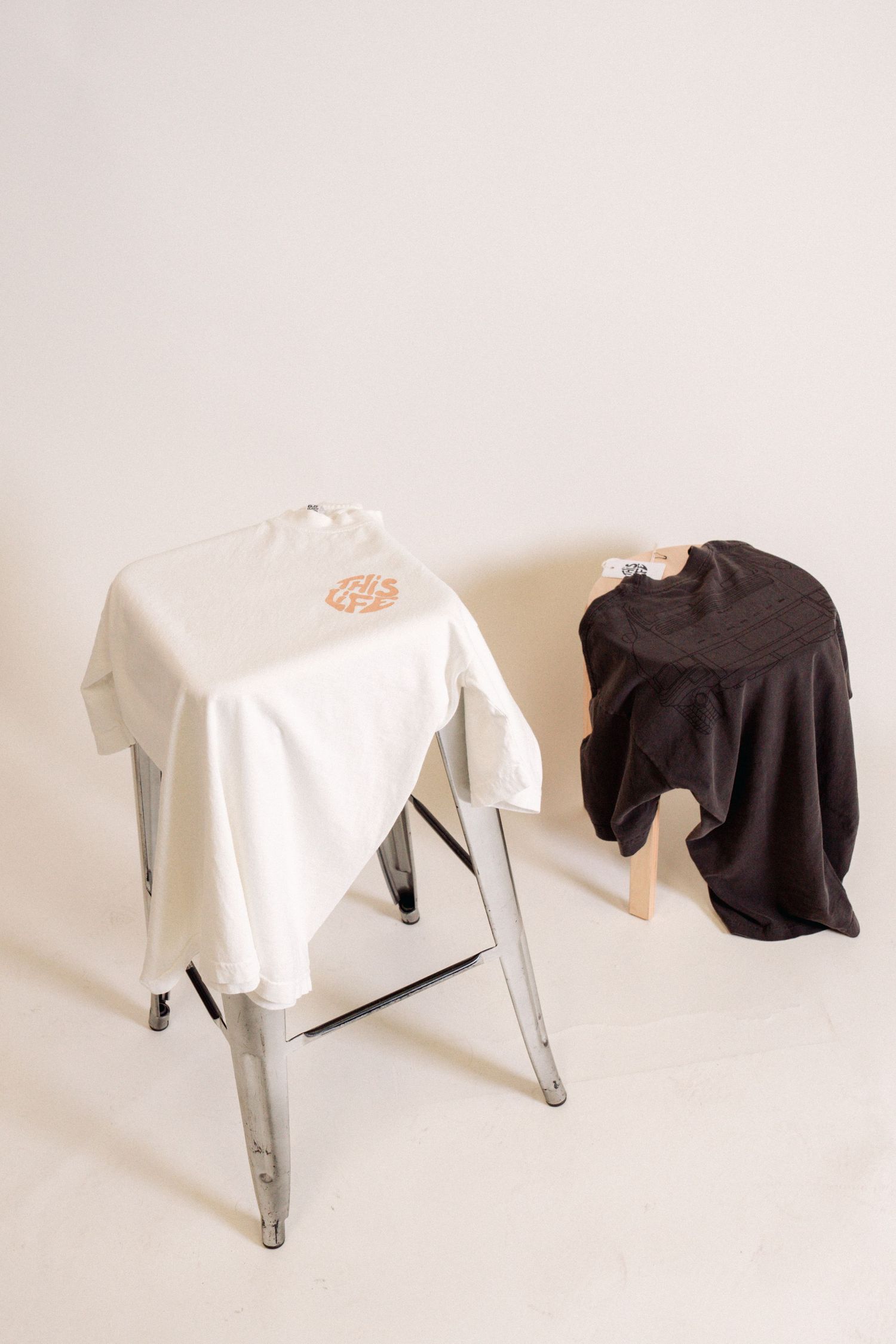 Black and white t-shirts displayed on metal stools against light background.