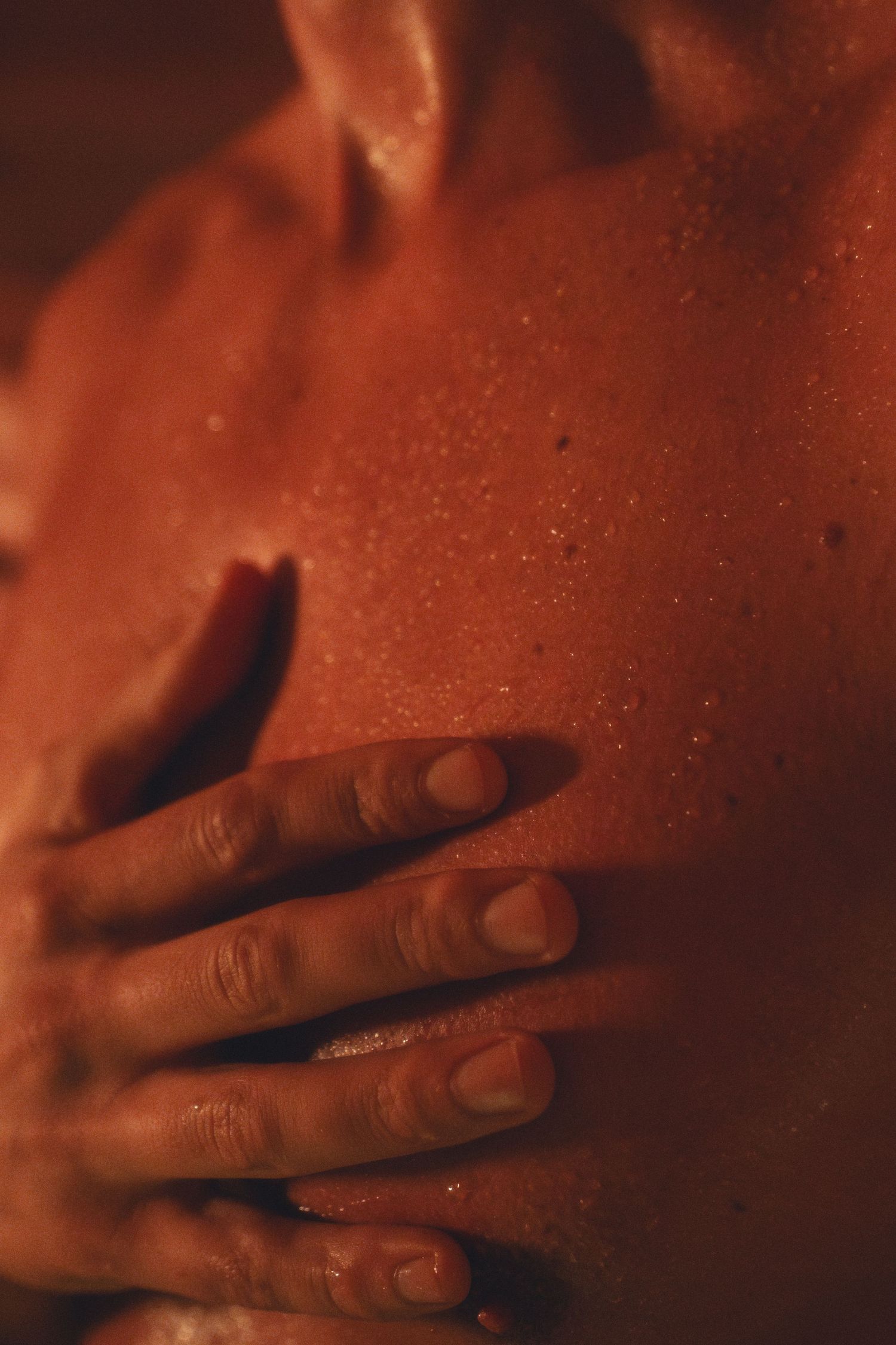 Close-up of a hand against skin in warm, amber lighting.