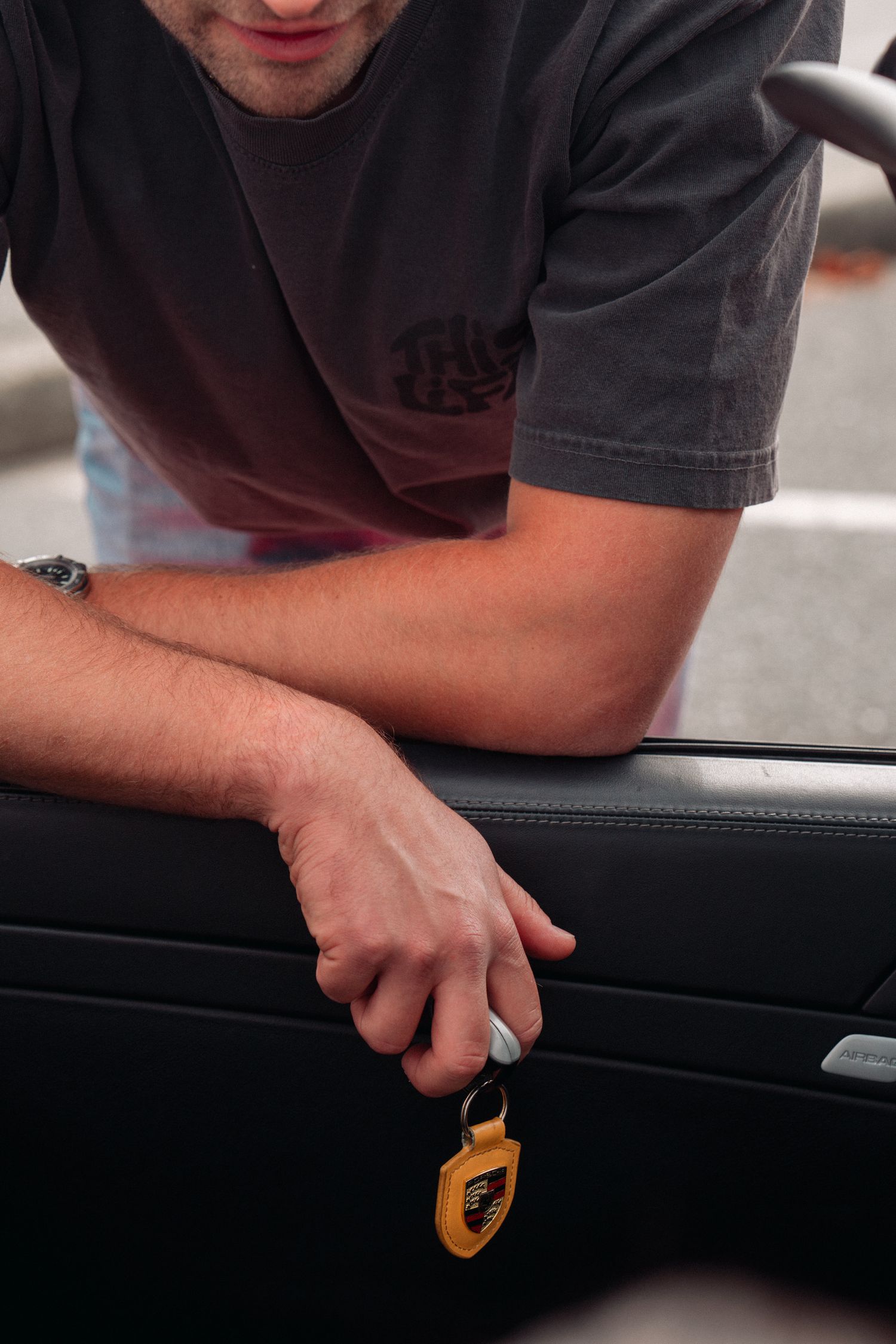 Close-up of hand holding car key with Porsche logo keychain.