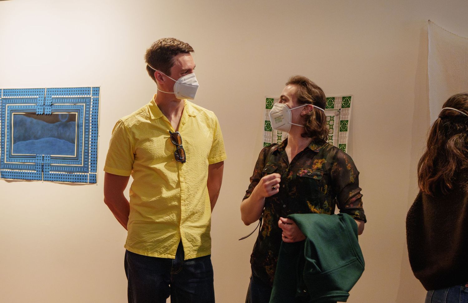 Small group discusses art in gallery space while wearing protective masks.