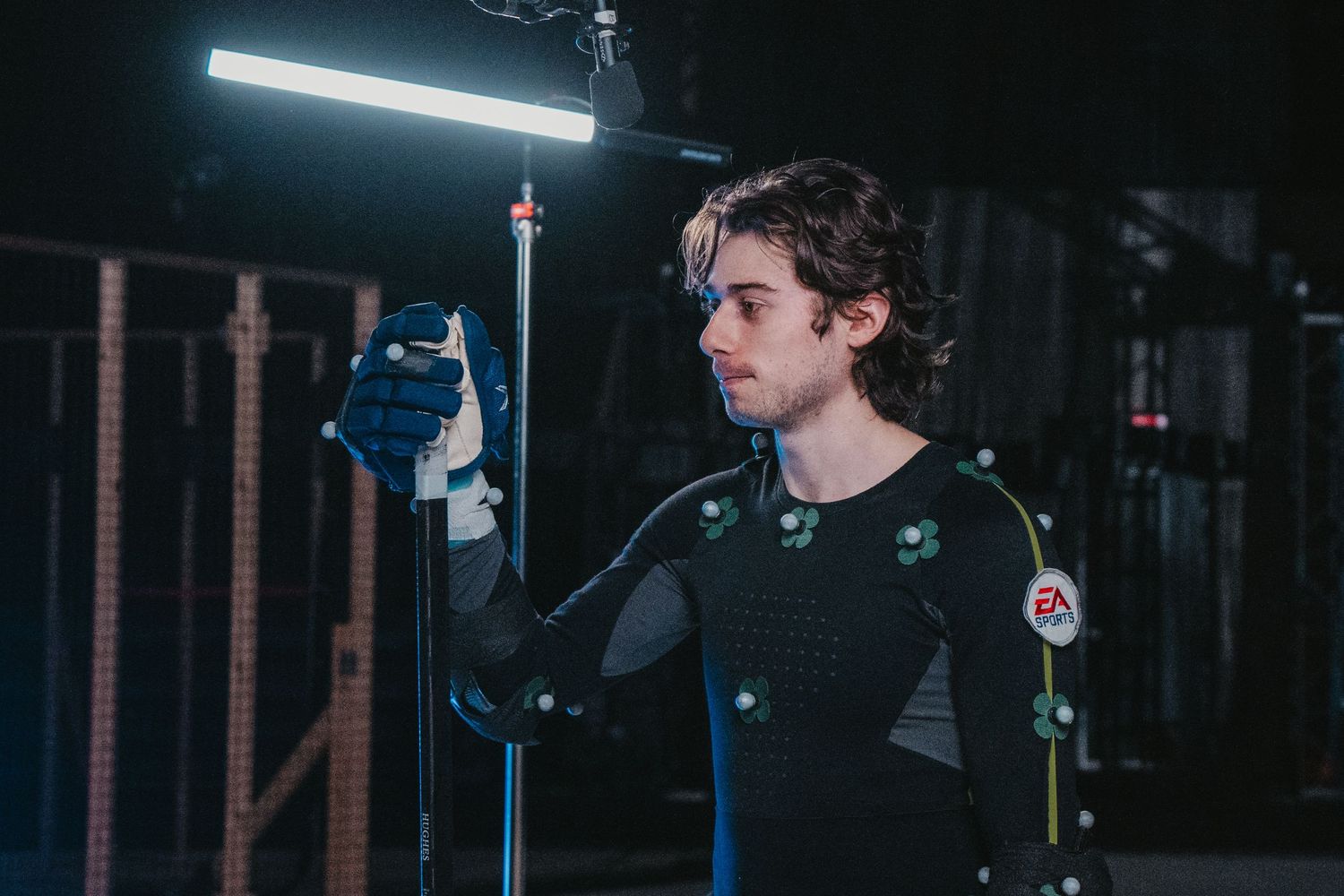 Performer in motion capture gear stands under lighting in a dark studio environment.