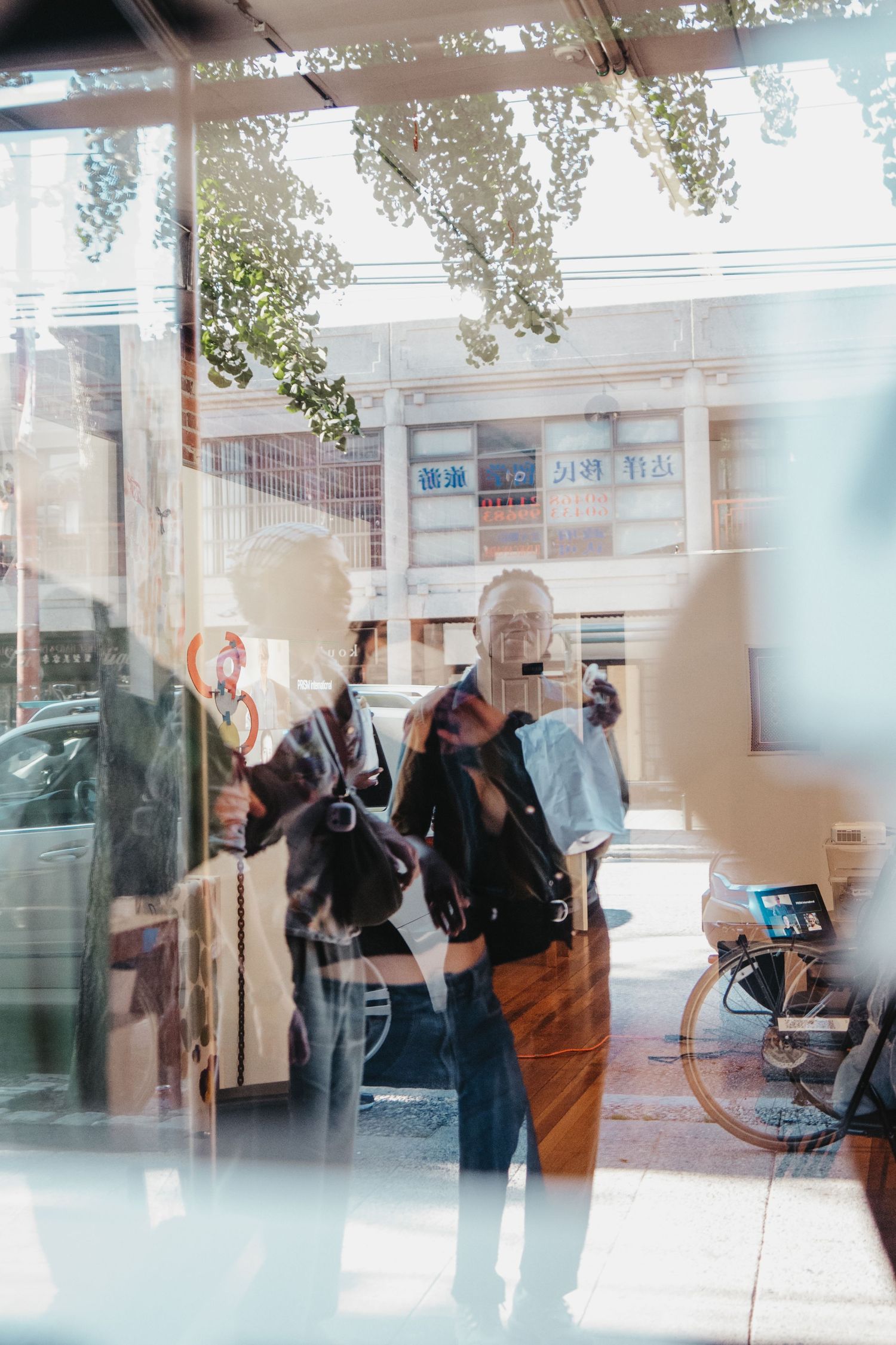 Through a window reflection, people gather inside what appears to be a retail or cafe space.