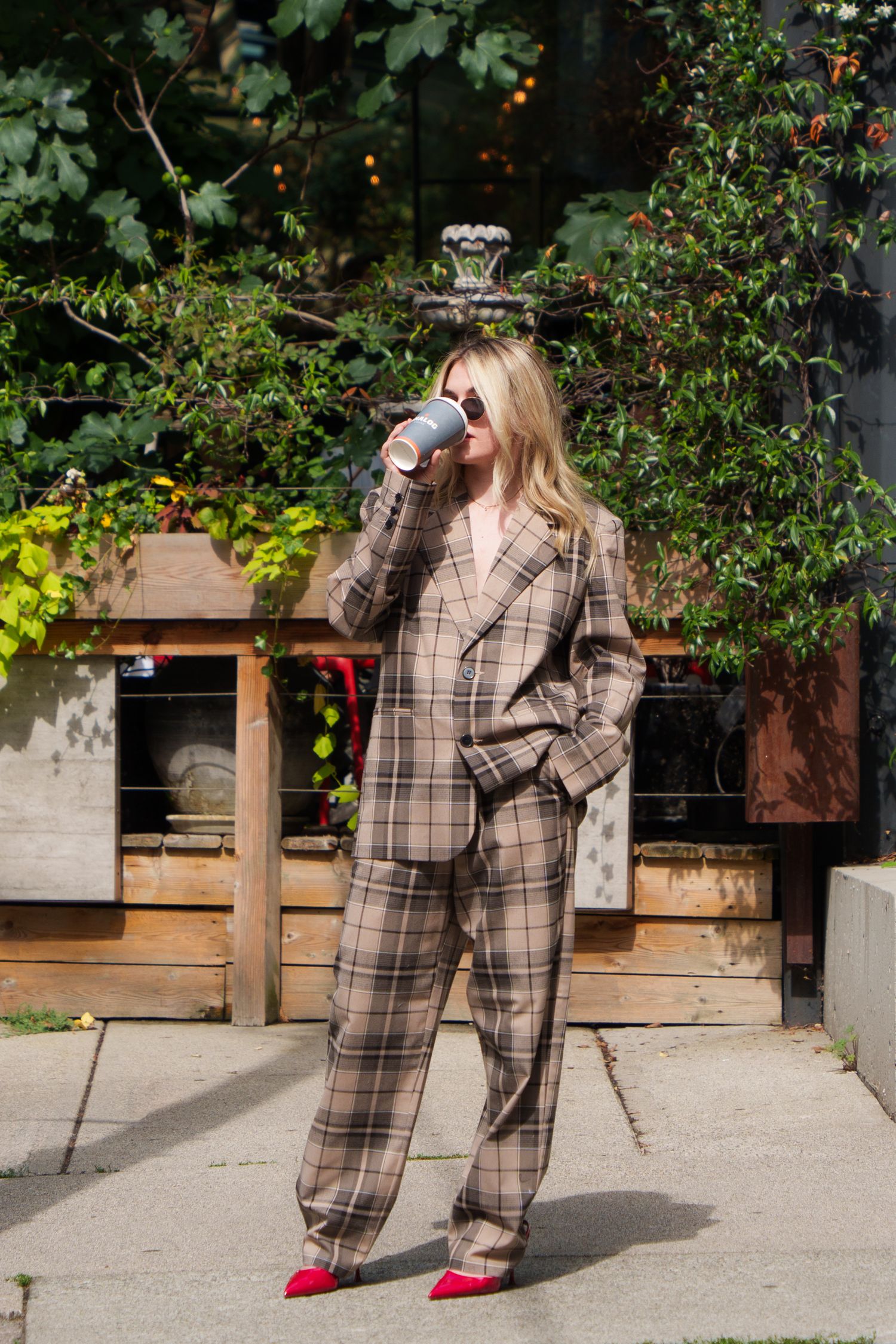 Person wearing plaid suit drinking coffee in garden setting with red shoes.