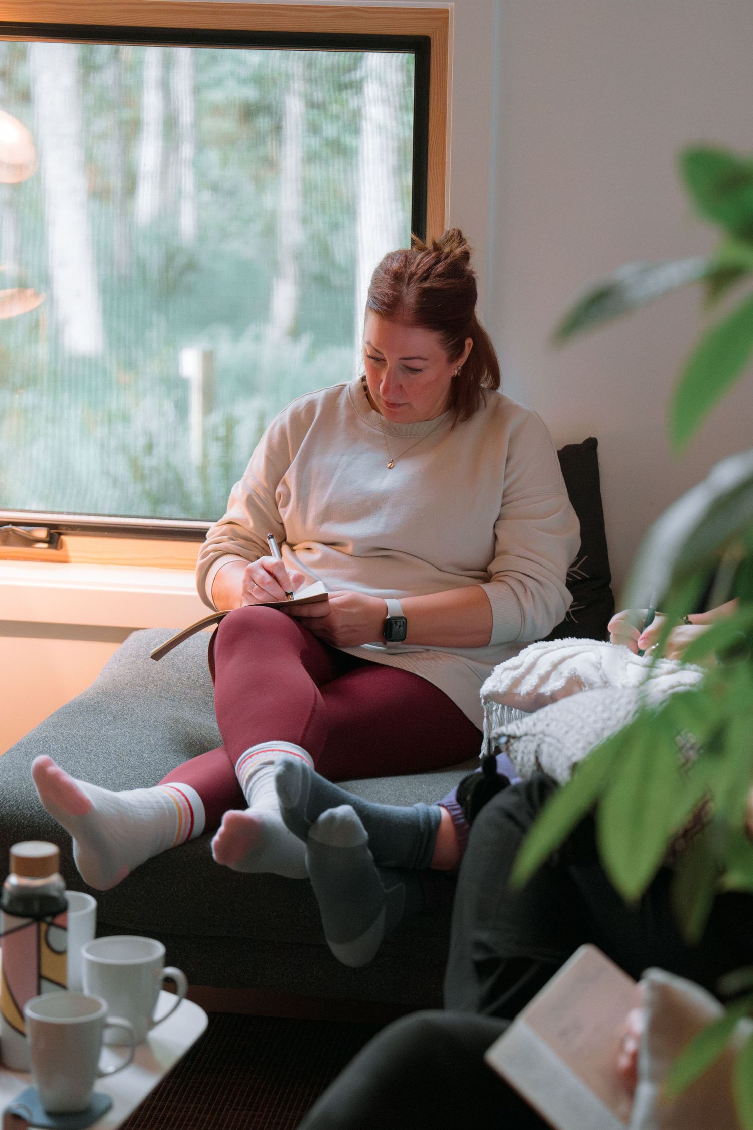Someone writing in a journal while sitting in a window seat with socks and comfortable clothing.