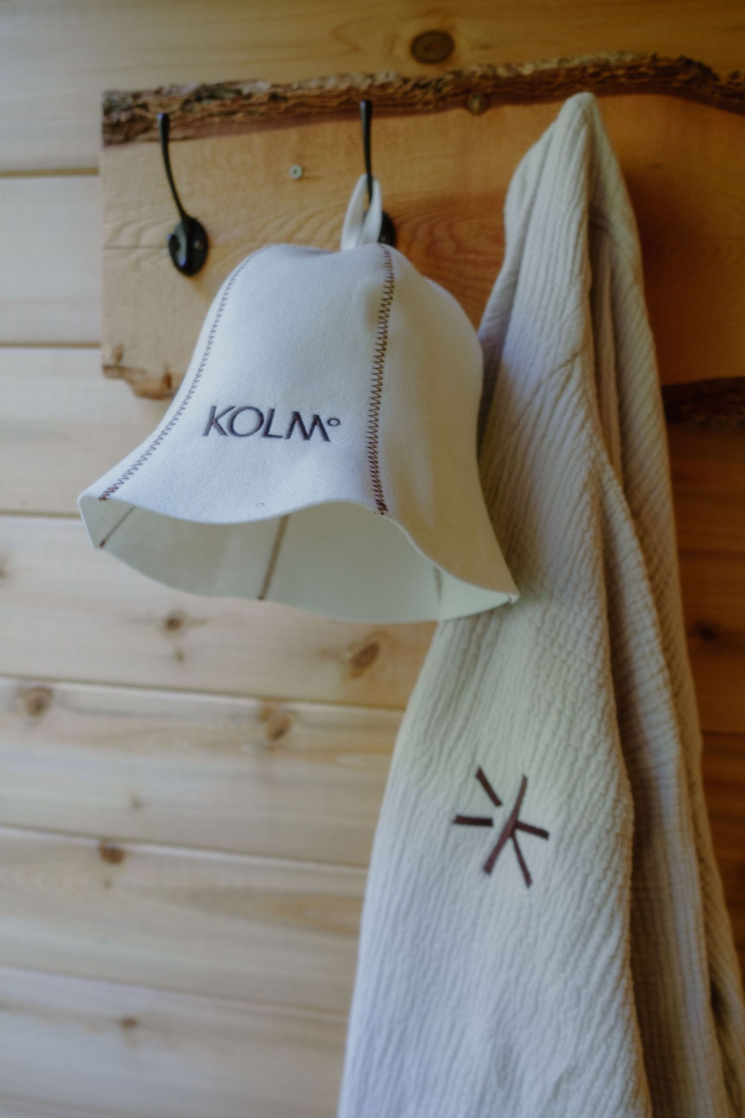 White Kolm sauna lamp and towel hanging on rustic wooden wall with natural wood details.