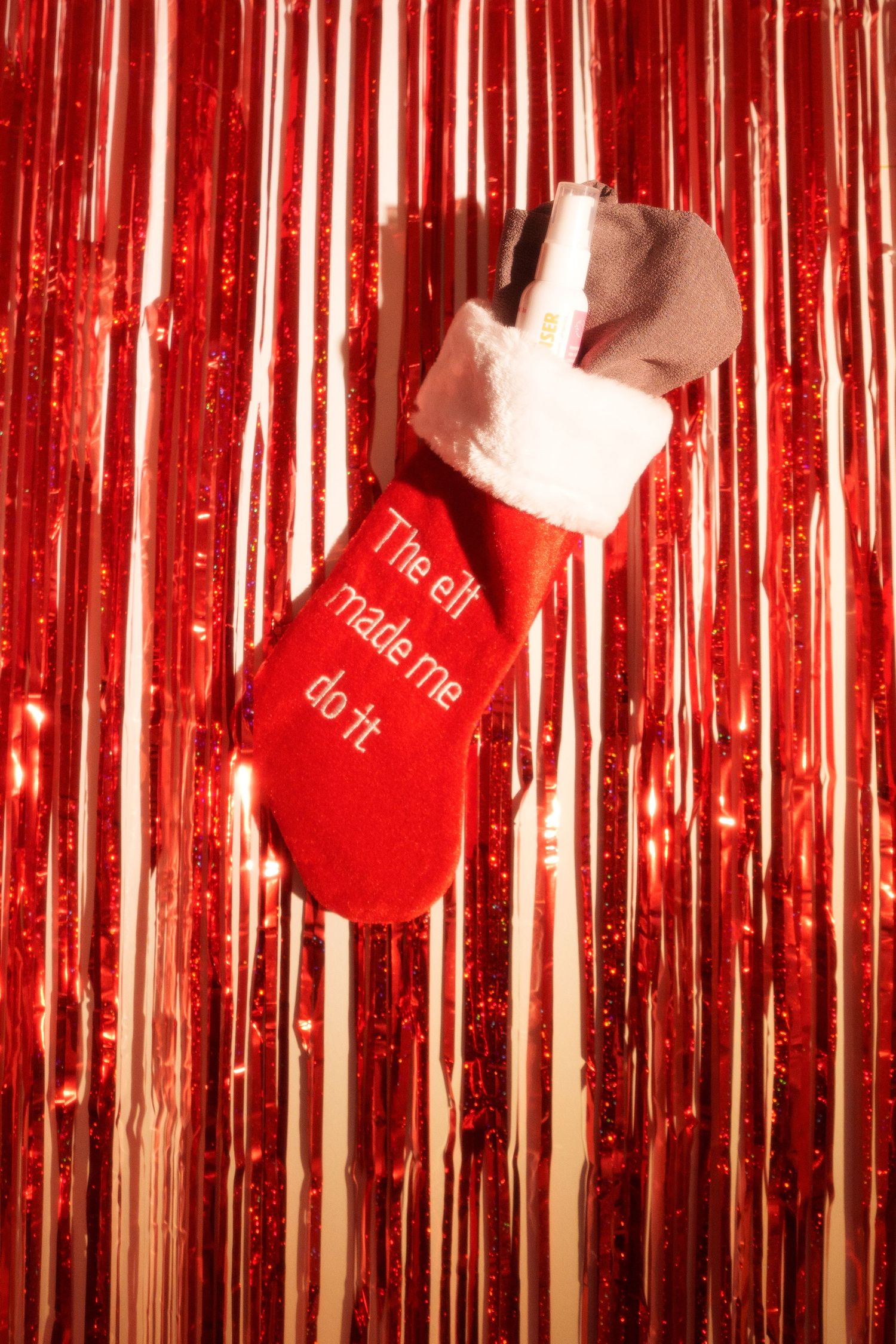 Red Christmas stocking with white trim hanging against shiny metallic tinsel backdrop.