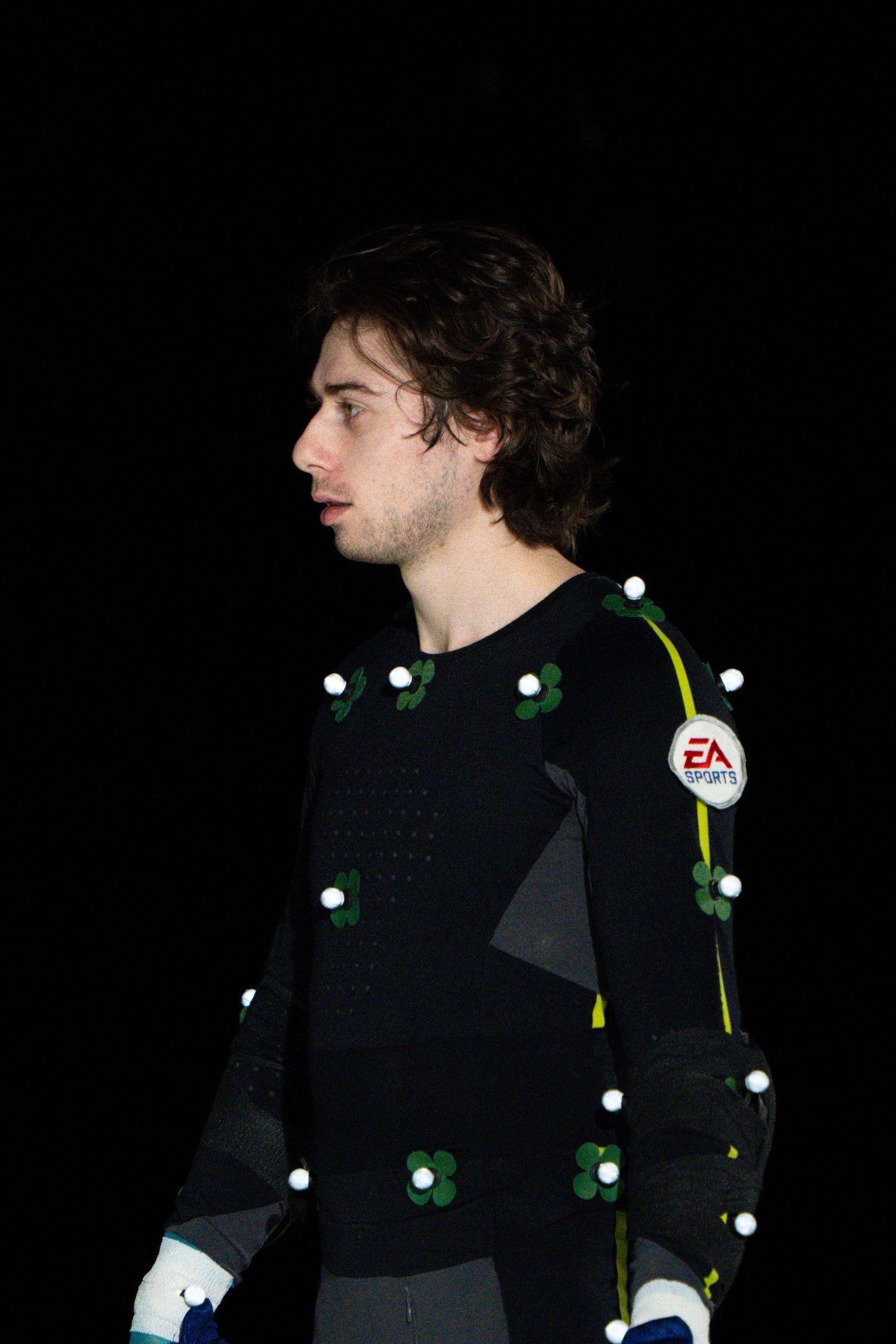 Profile view of performer wearing black motion capture suit with glowing tracking markers.