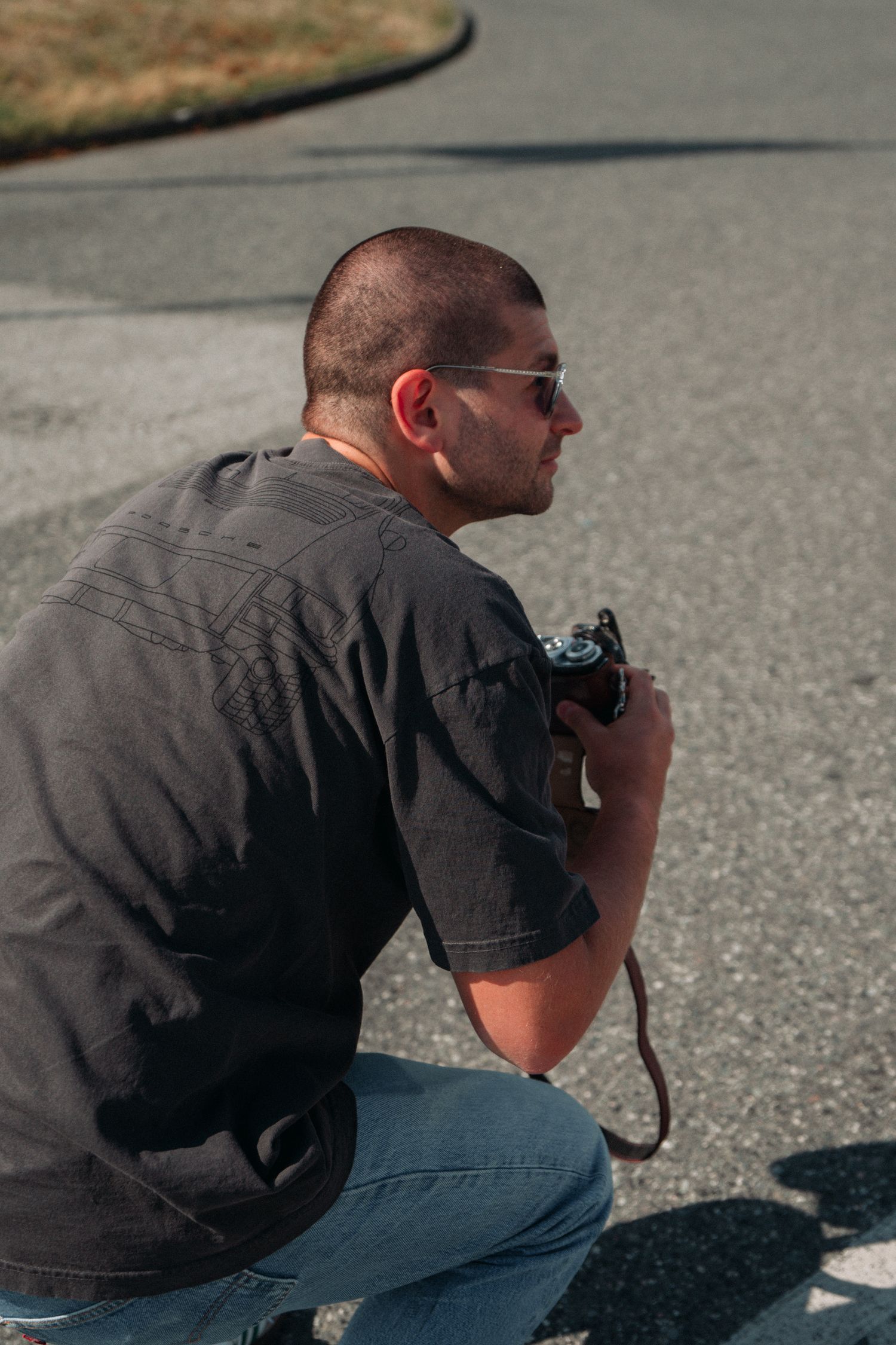 A photographer crouching with camera in hand on an asphalt road.