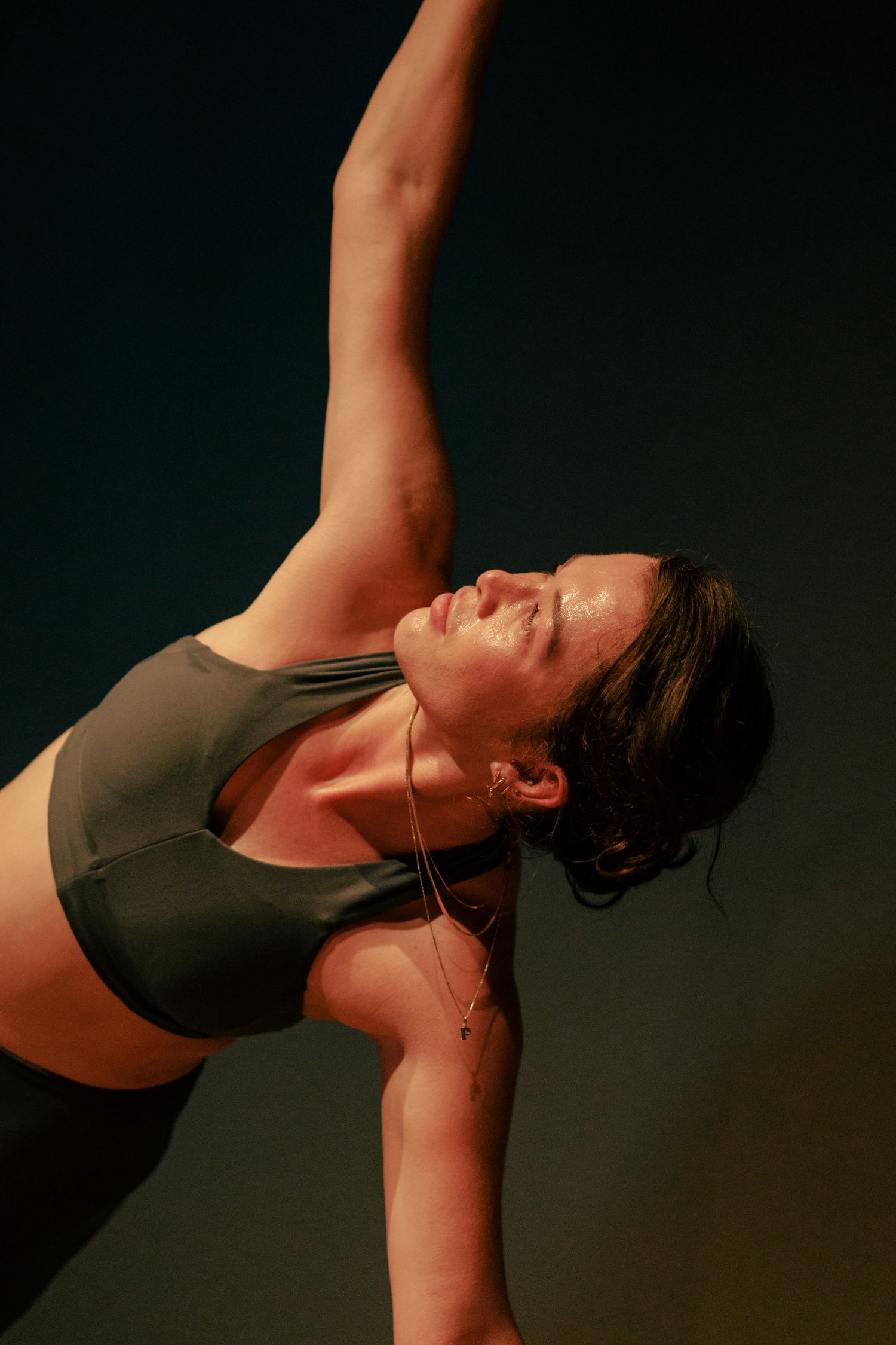 Athletic dancer in a black sports bra performs a graceful side bend stretch against dark background.
