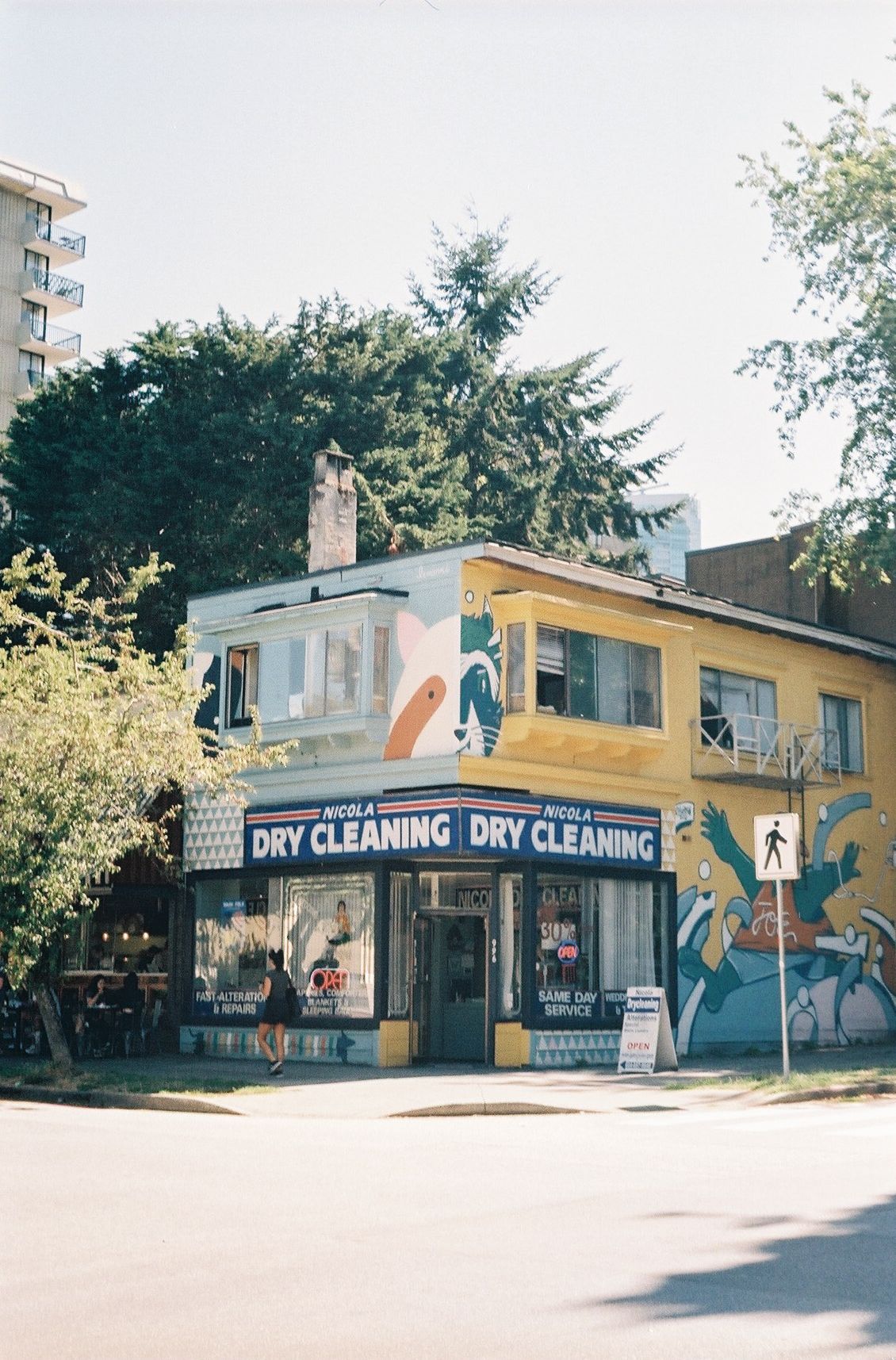 Yellow corner building with dry cleaning storefront and colorful street art mural.