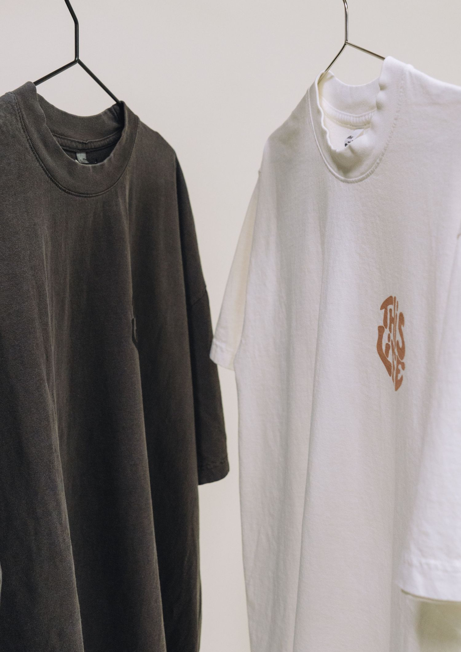 Two t-shirts hanging on display, one black and one white with logo details.