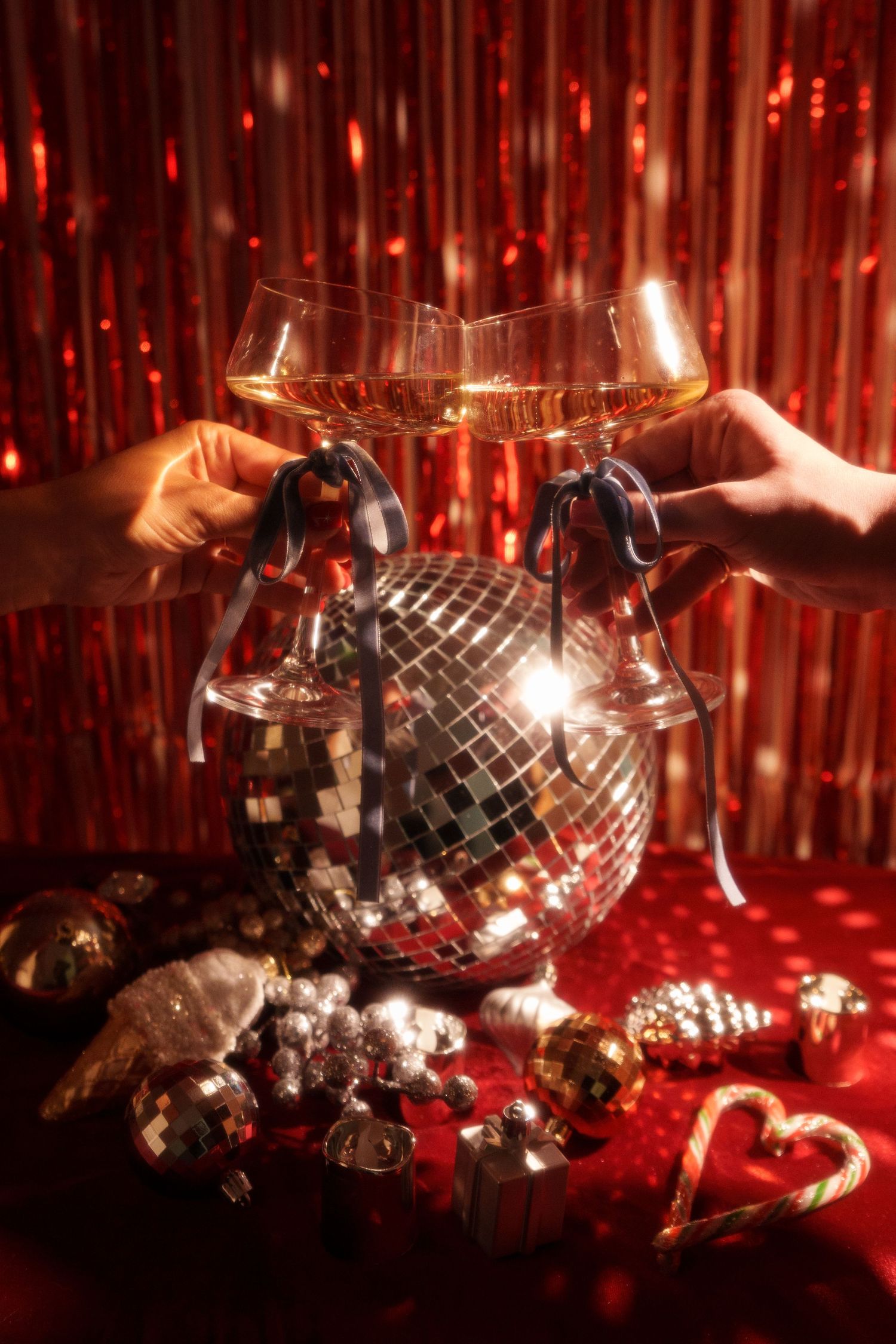 Two champagne glasses toasting in front of disco ball with red sparkly backdrop.