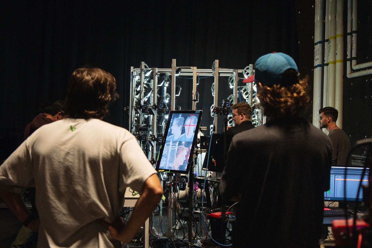 Production crew reviewing equipment and monitors on a dark film set.