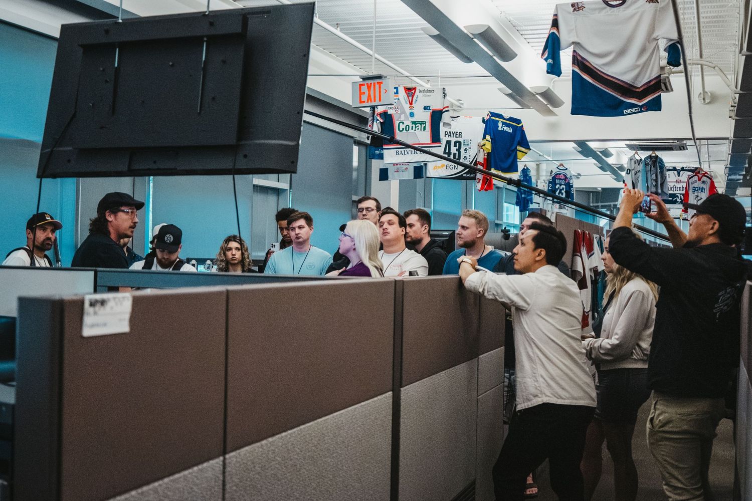 Office workers gather around cubicle walls during a casual workplace interaction.