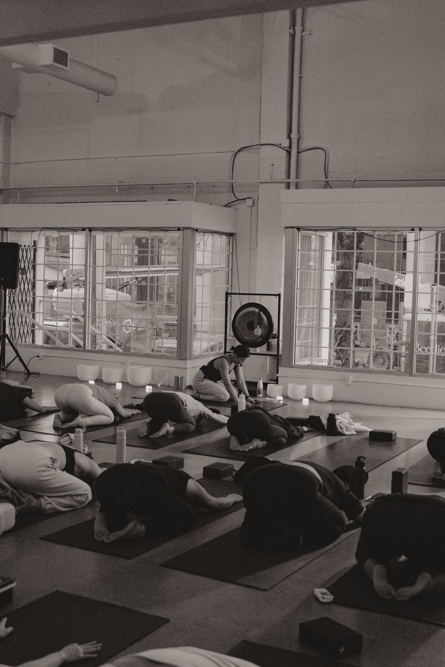 Students lie on mats during a group fitness or relaxation class in a bright studio with large windows.