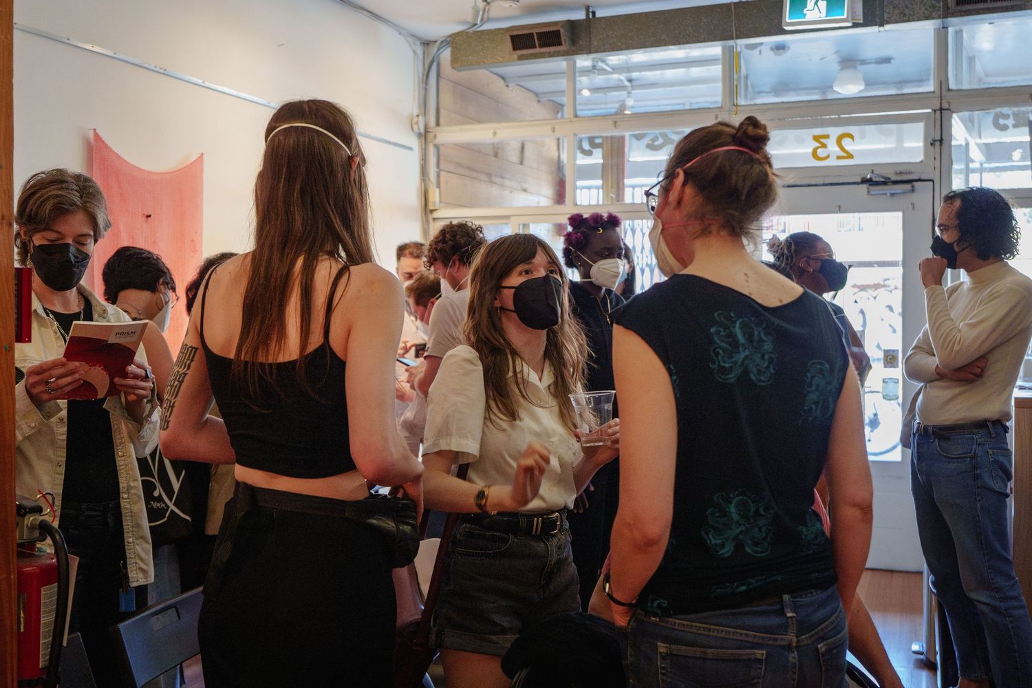 People gather in casual indoor space wearing masks and engaging in conversation.