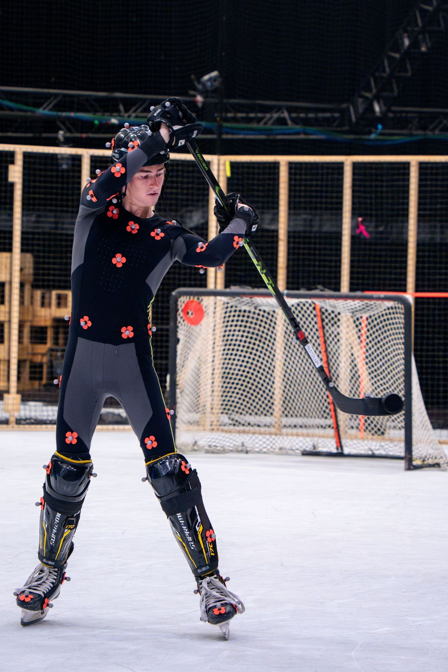 Performer in motion capture suit with tracking markers demonstrates hockey stance on white studio floor.