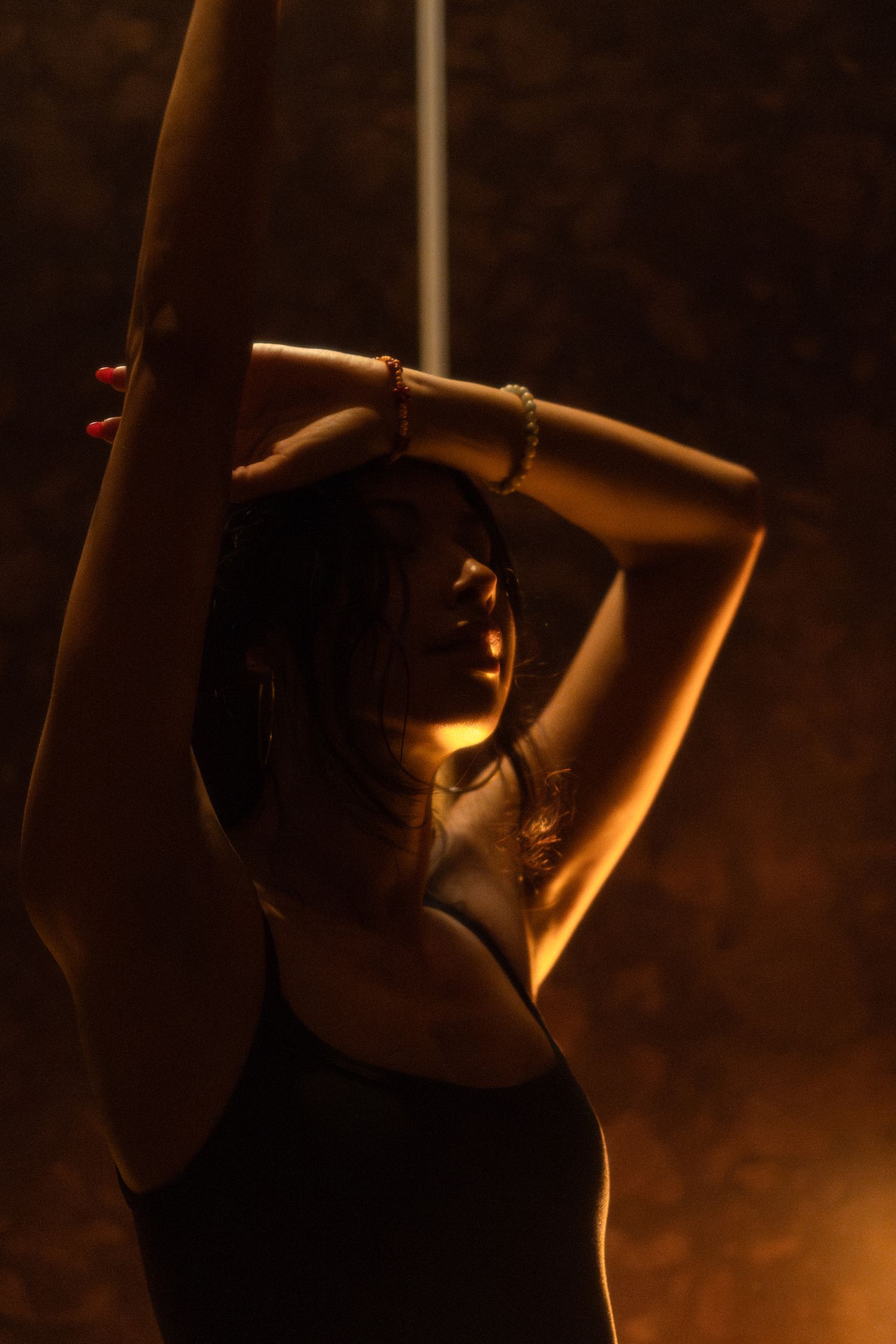 Artistic portrait of a dancer in warm lighting with arms raised overhead.